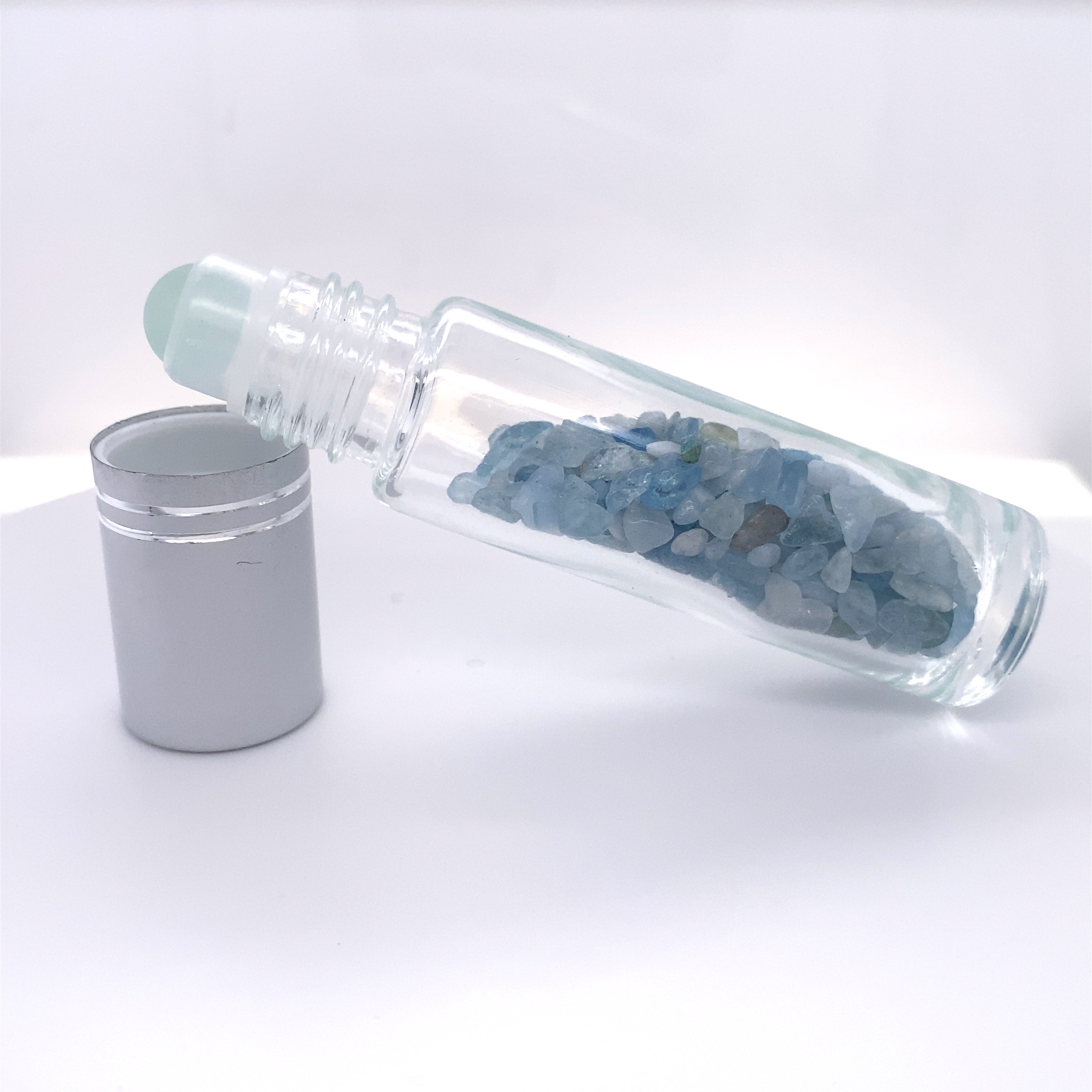 A glass bottle with blue crystals and a tin can next to it, perfect for self care relaxation or Stone Essential Oil Roller storage.