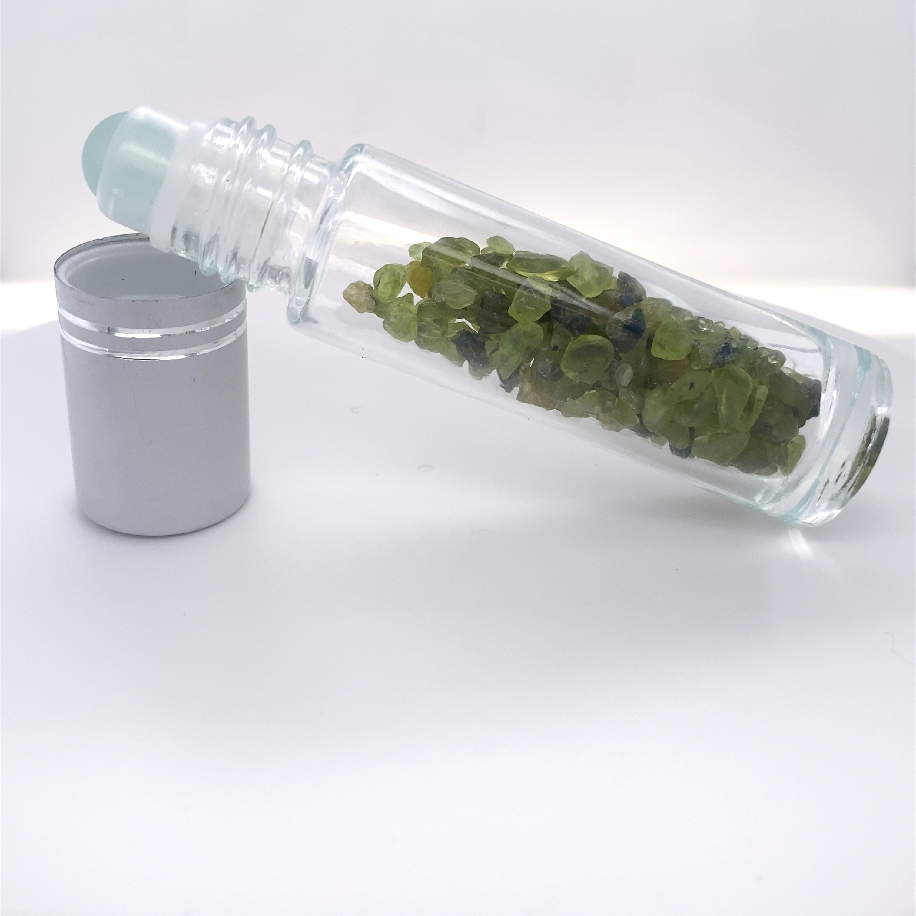 A glass bottle filled with beauty-enhancing green leaves, accompanied by a Stone Essential Oil Roller.