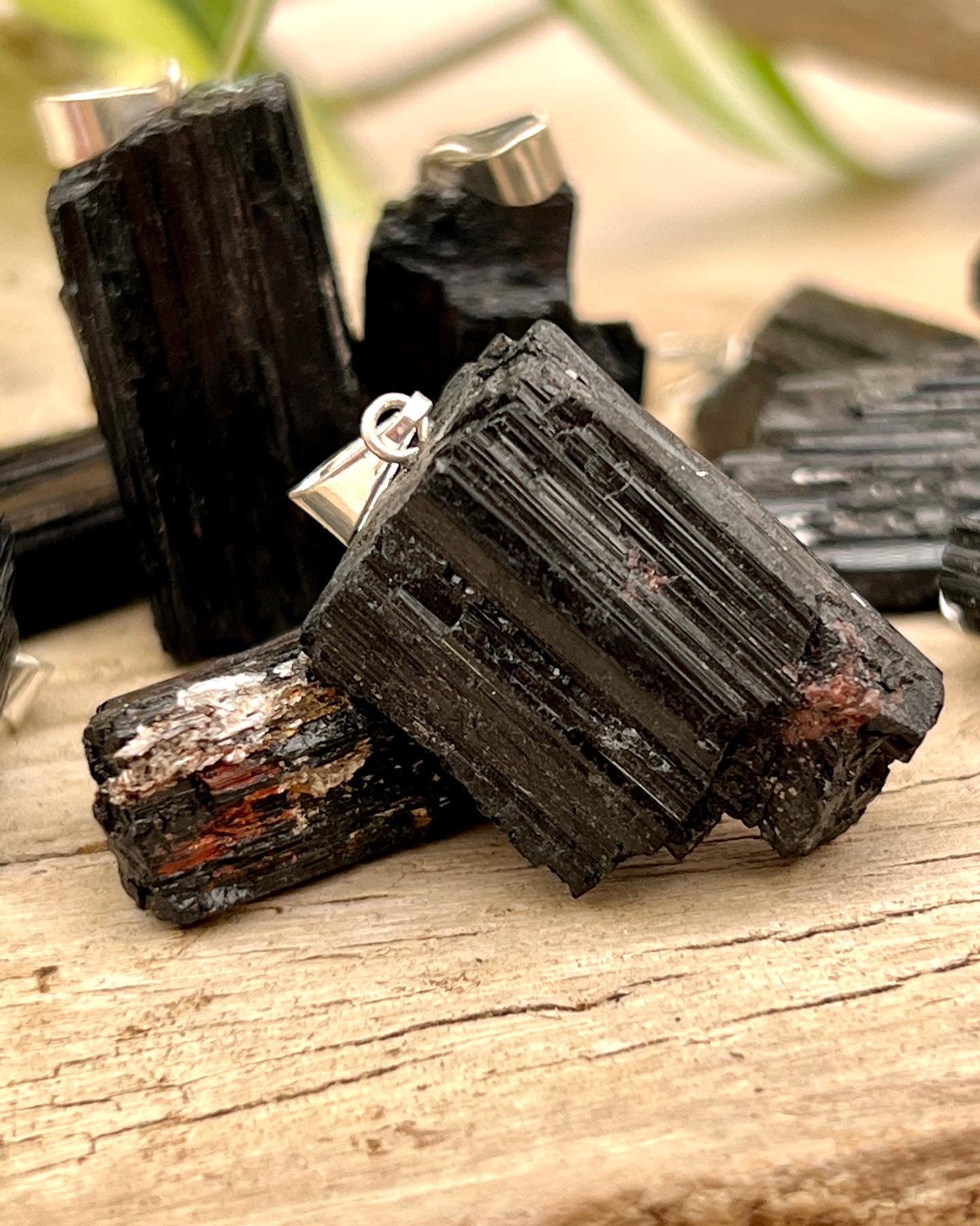 Super Silver's Raw Crystal Pendants, including black tourmaline, on a wooden table.