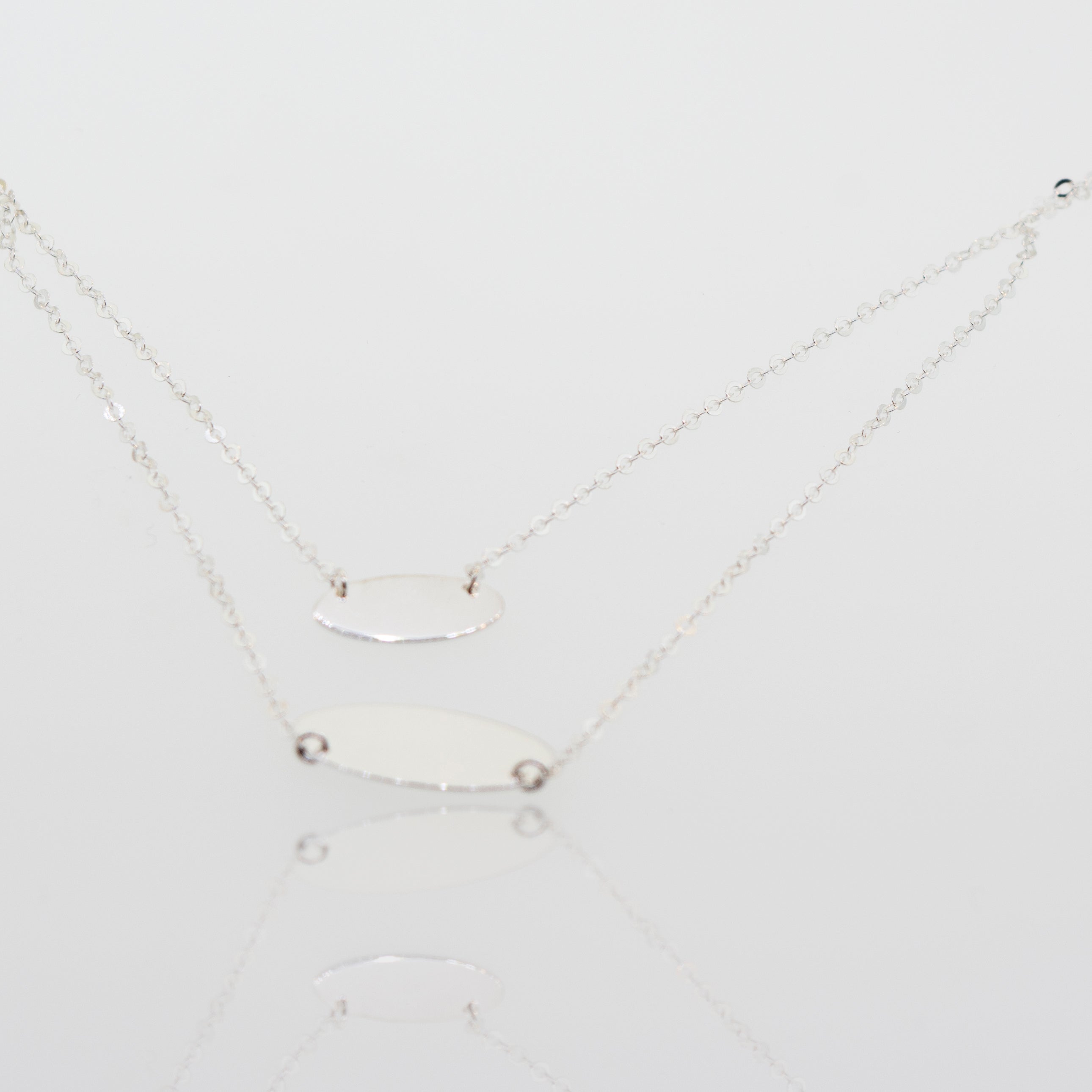 Two adjustable Super Silver sterling silver necklace with oval discs pendants on a white surface.