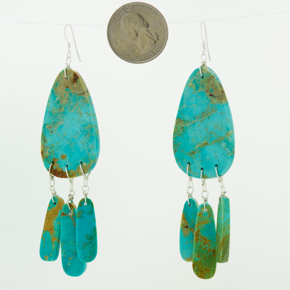 A pair of Super Silver Native American Raw Turquoise Earrings elegantly dangle beside a coin.