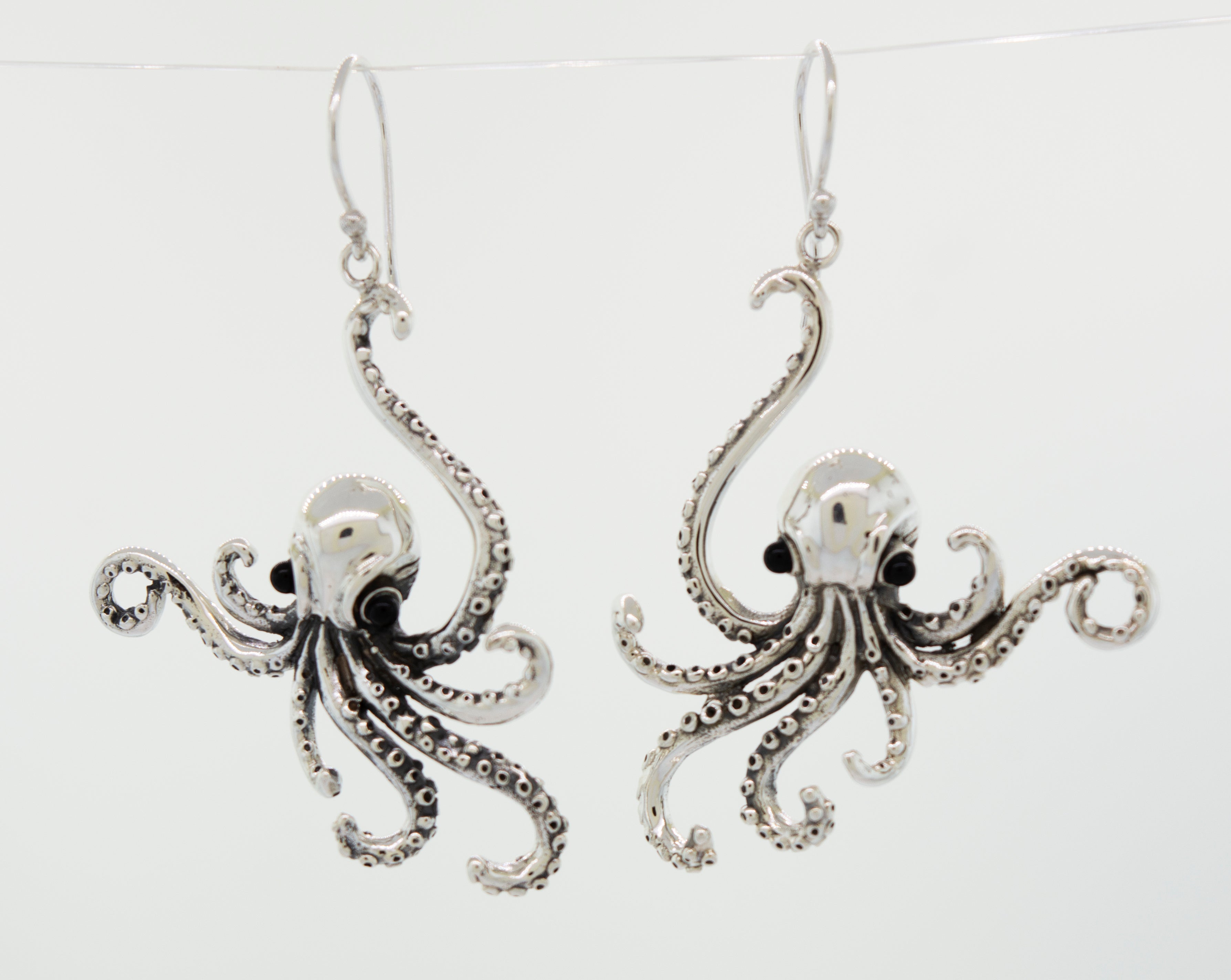 A pair of Super Silver Designer Octopus Earring with Onyx Eyes, delicately hanging from a wire.