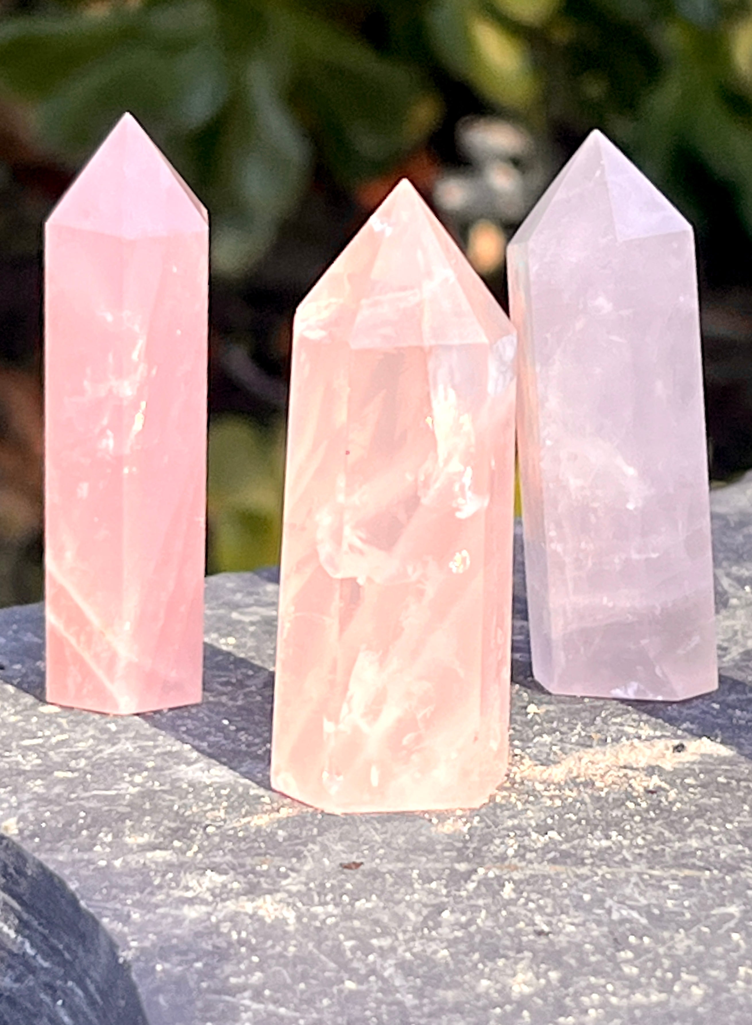 Three Rose Quartz Obelisks sitting on top of a stone.