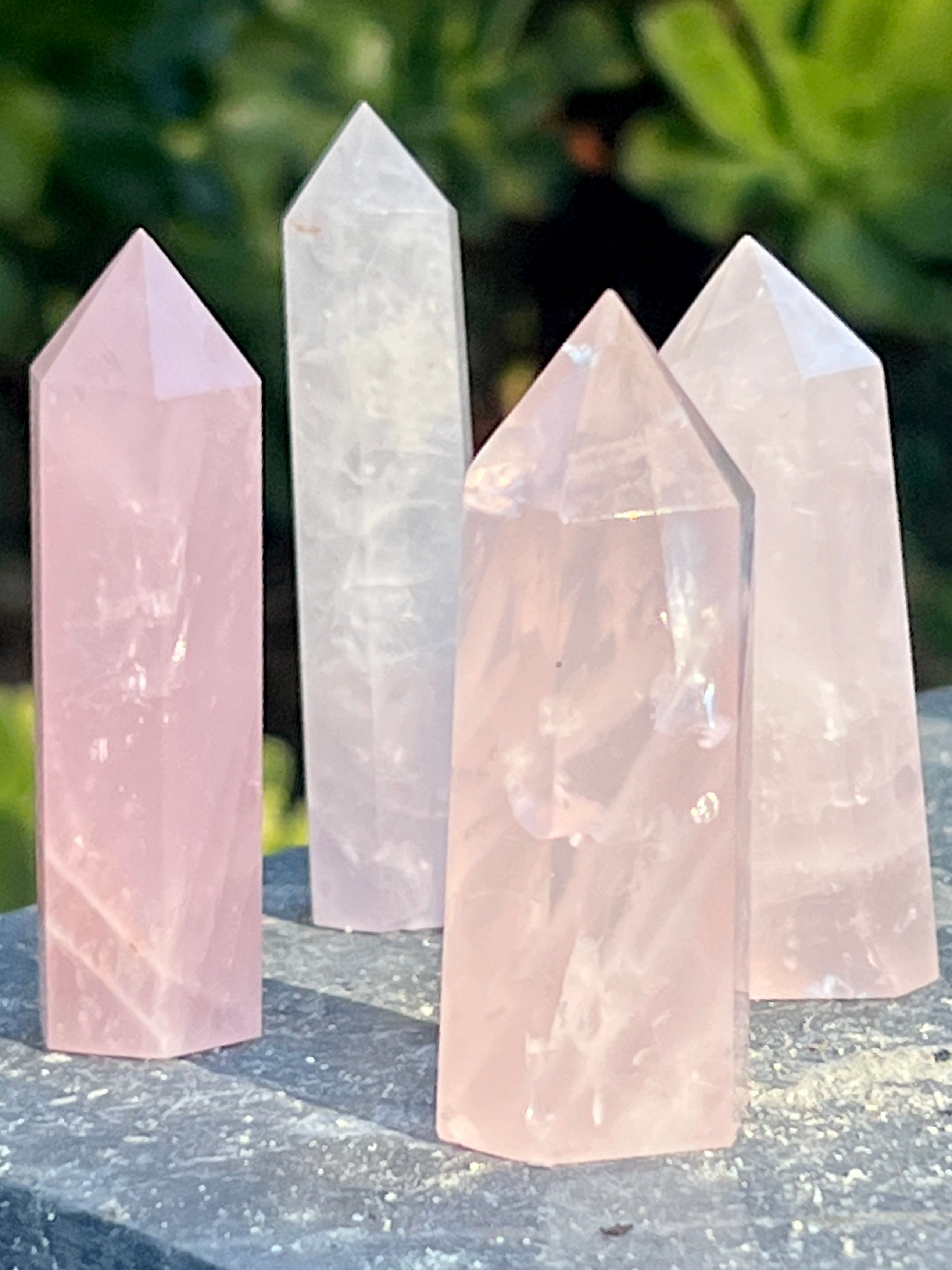 Three Rose Quartz Obelisks arranged decoratively on top of a rock.