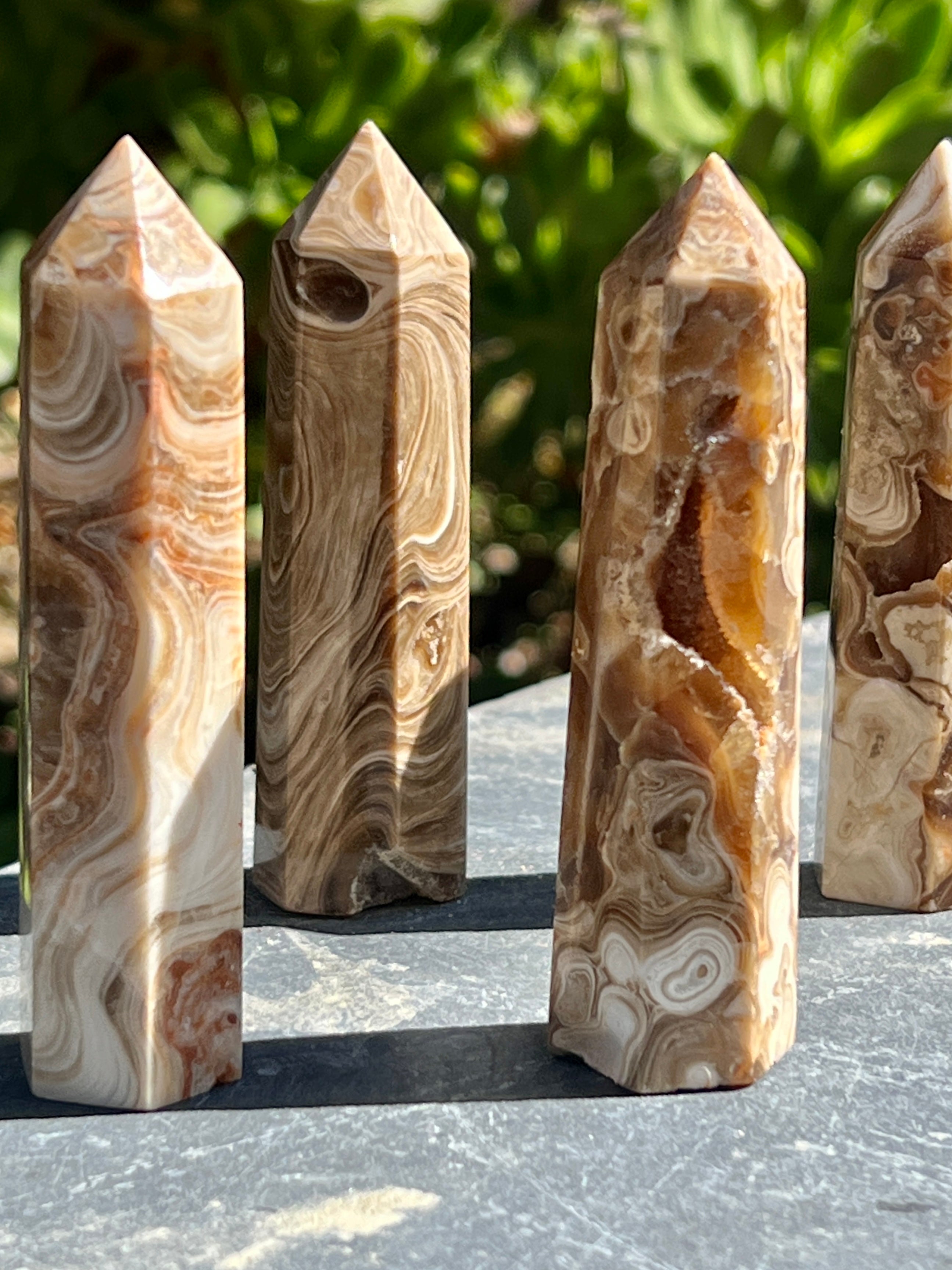 Four Brown Aragonite Obelisks on a table in front of a garden, serving as elegant decor.