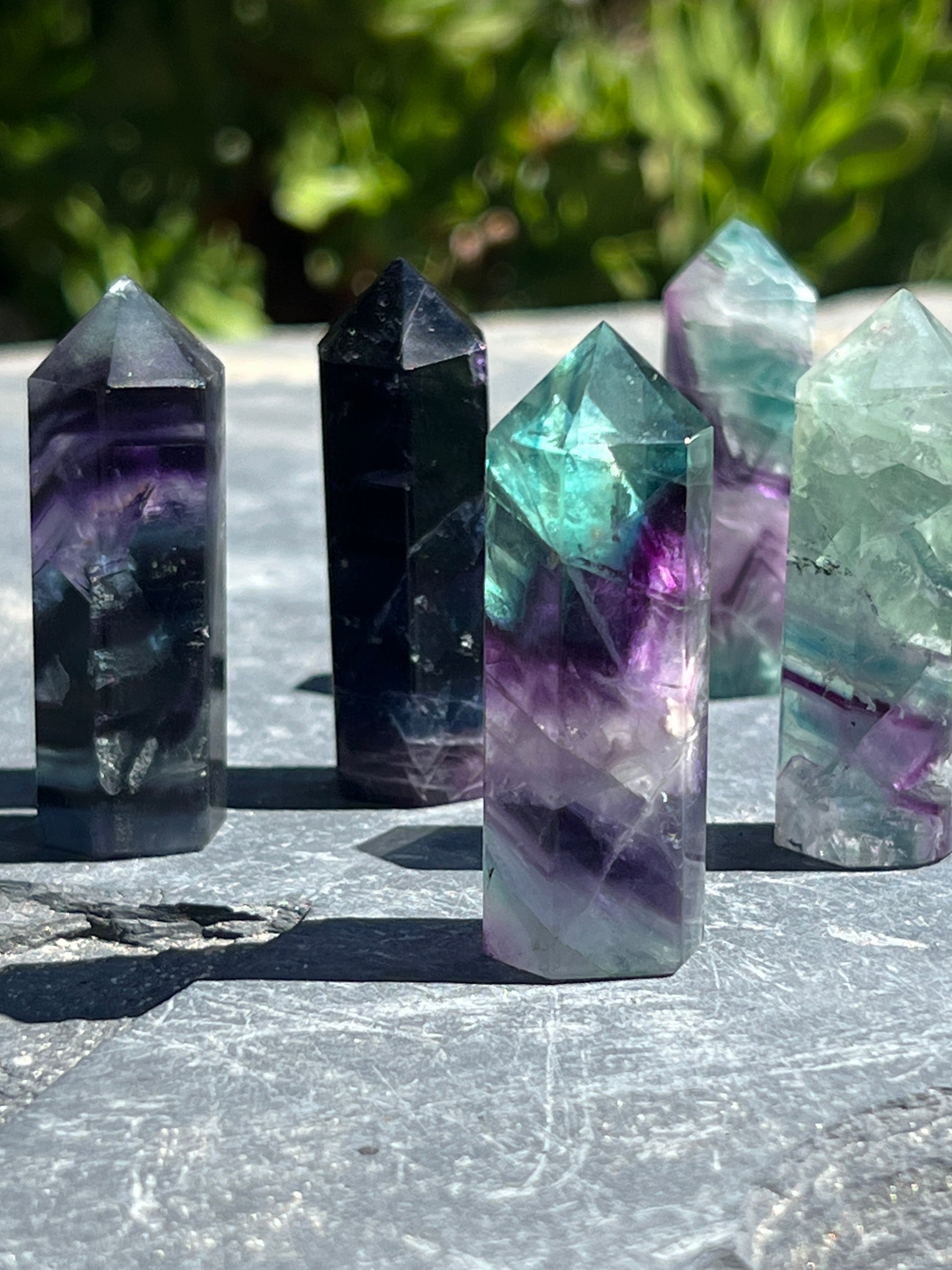 A Rainbow Fluorite Obelisk on a stone slab, perfect for decor enthusiasts seeking a touch of green or purple in their space.