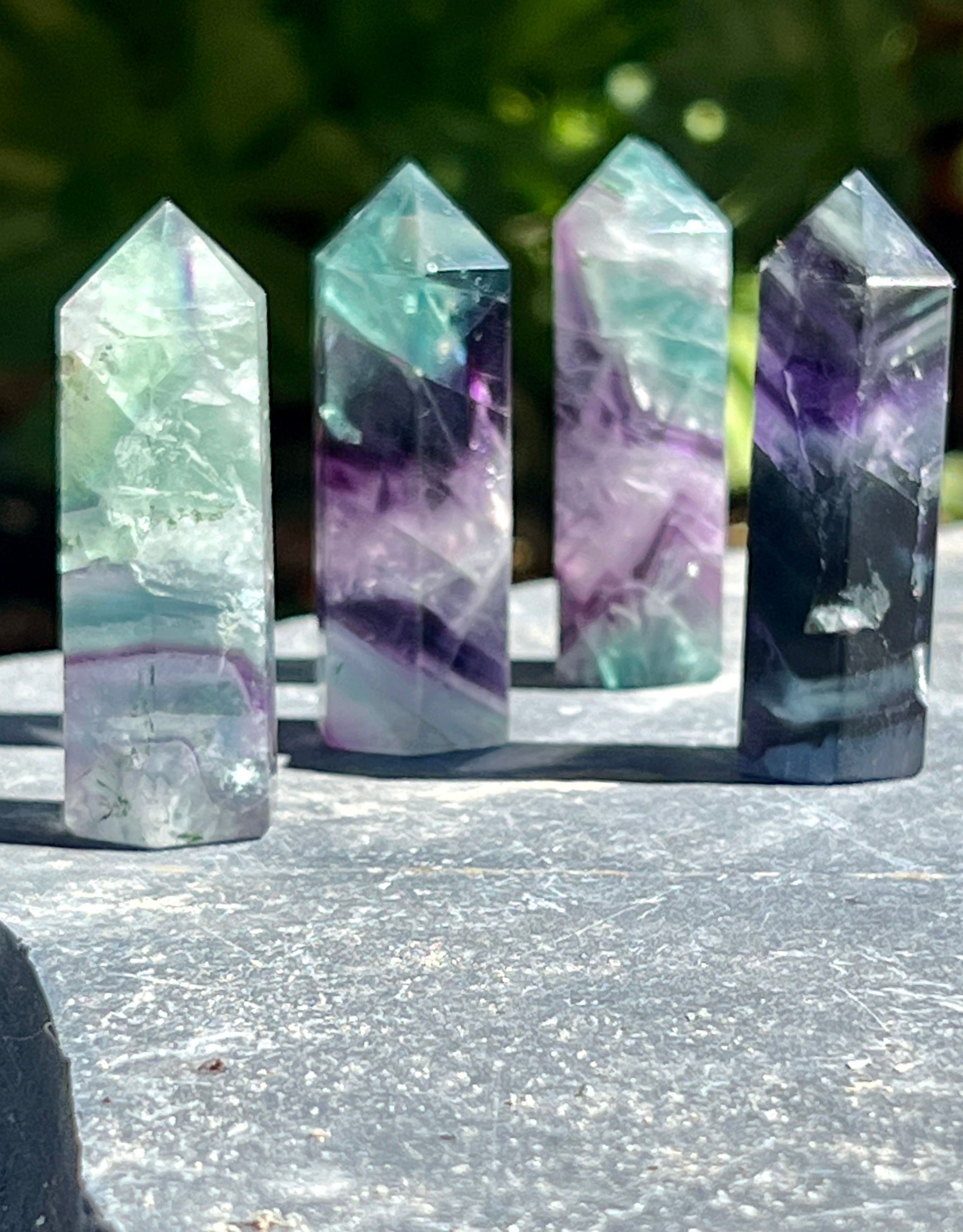 A Rainbow Fluorite Obelisk on a stone table.
