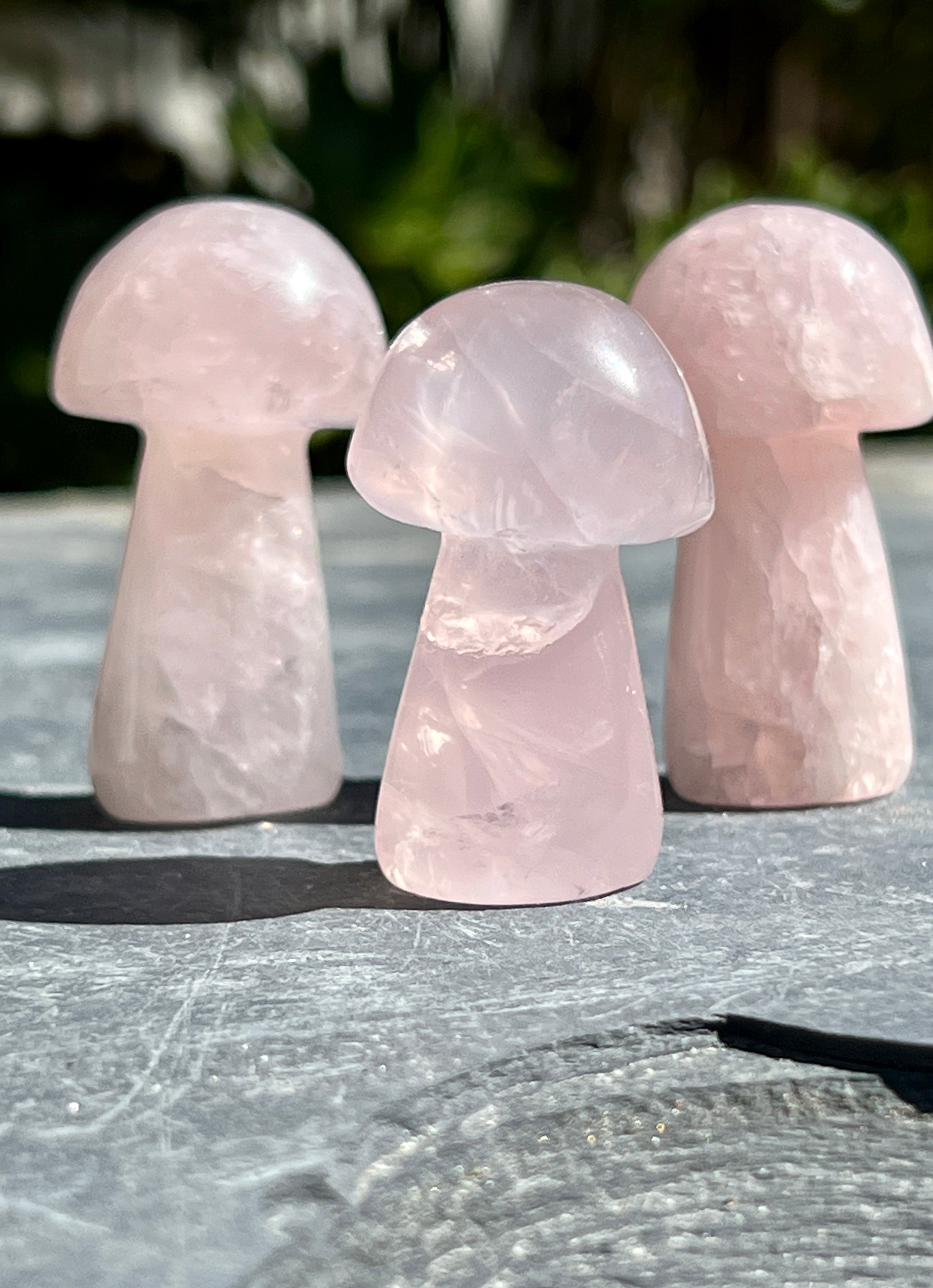 Three rose quartz mushrooms on a crystal-decorated stone table.
