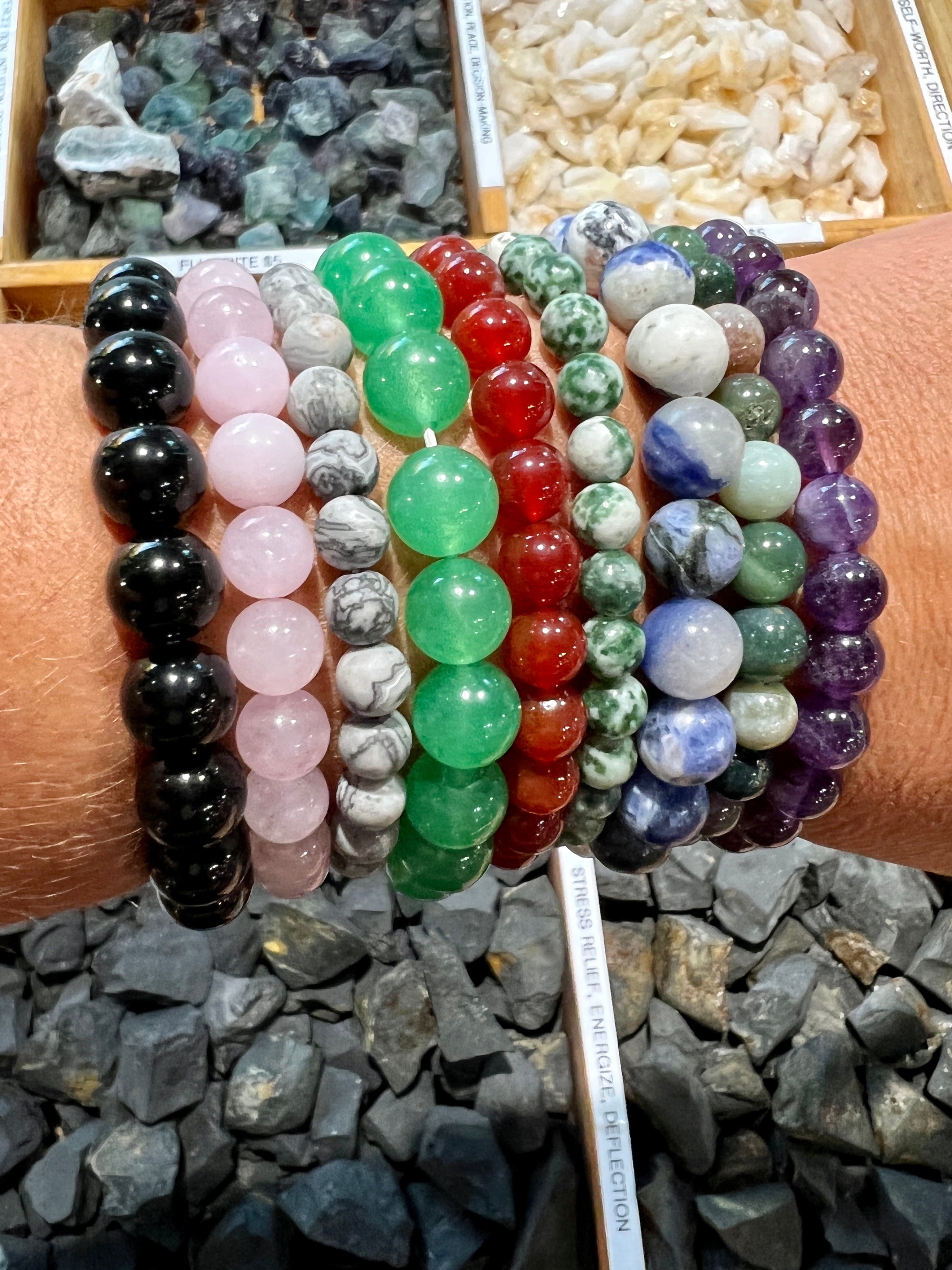 A woman's hand is holding a variety of Super Silver Beaded Stone Bracelets.