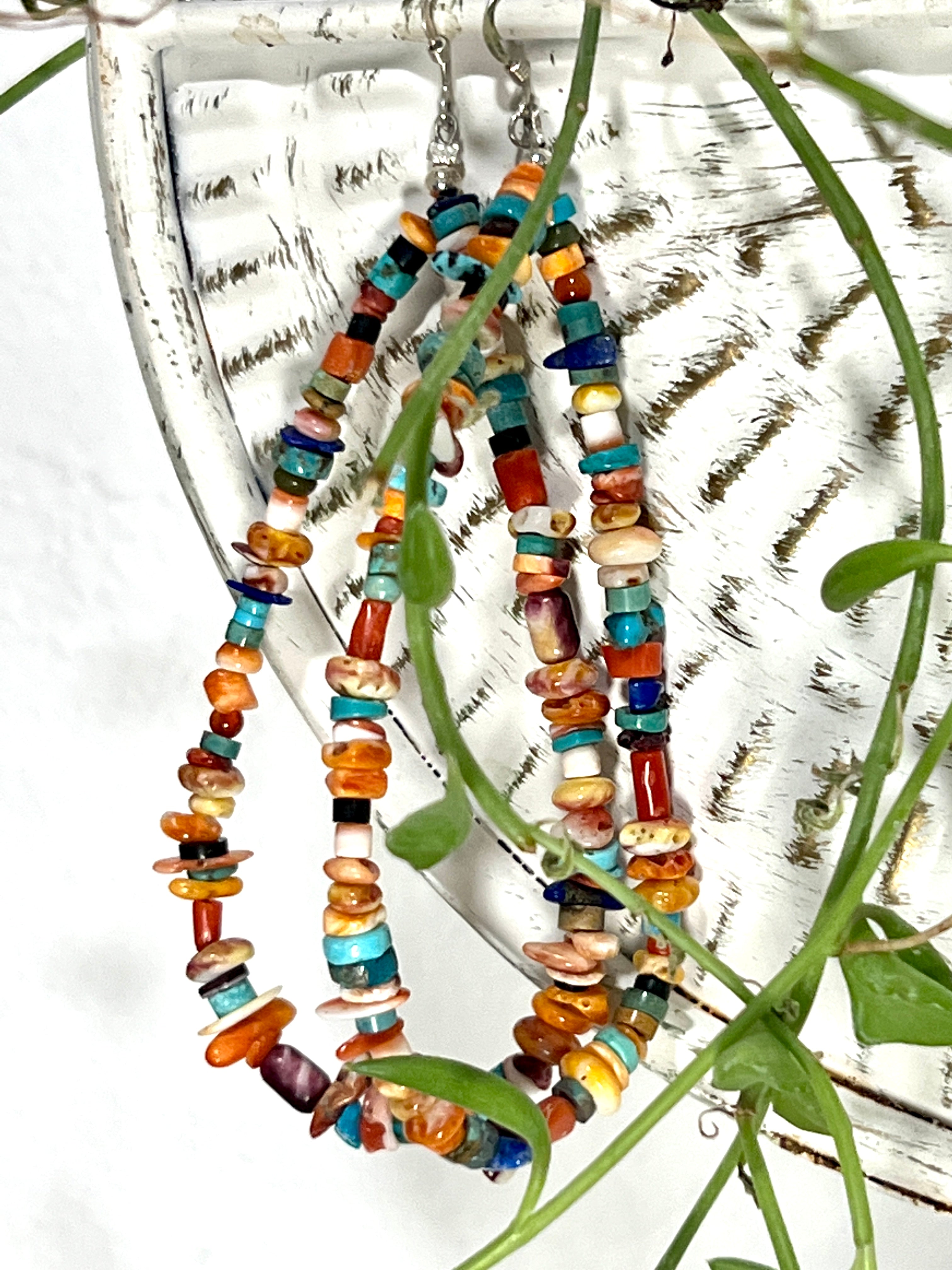 A pair of Brilliant Southwest Beaded Earrings by Super Silver, handmade statement earrings in southwest sunset colors, hang gracefully on a plant.