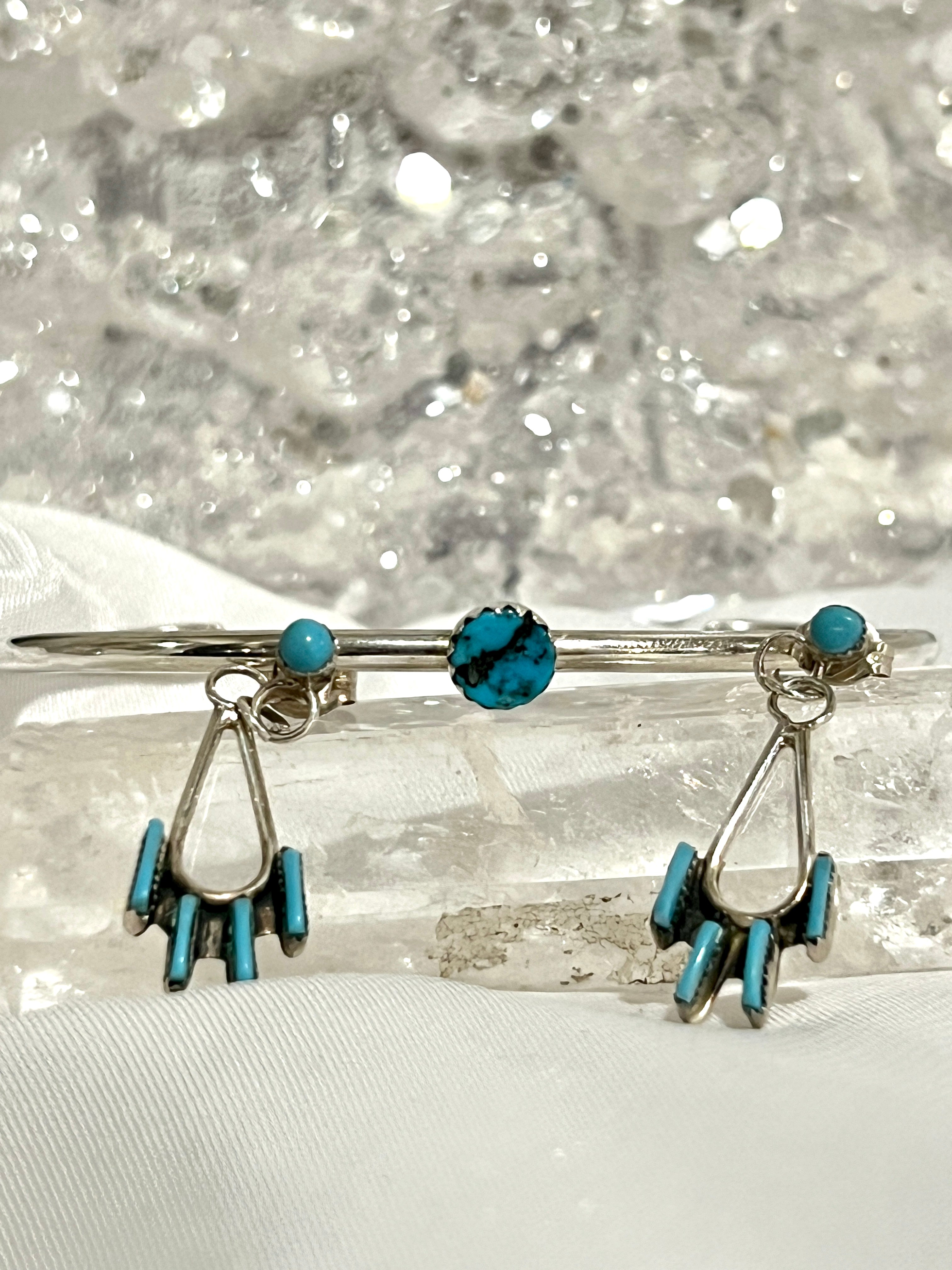 A pair of Delicate Needlepoint Zuni Turquoise Earrings by Super Silver with turquoise stones on top of a crystal.