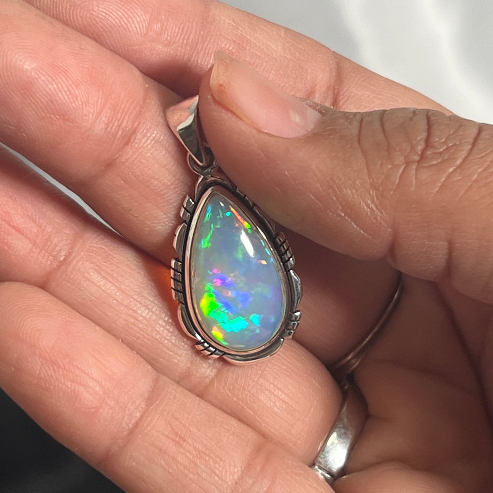 
                  
                    A person holding a Super Silver Ethiopian Opal Teardrop Shaped Pendant with Detailed Setting in their hand.
                  
                