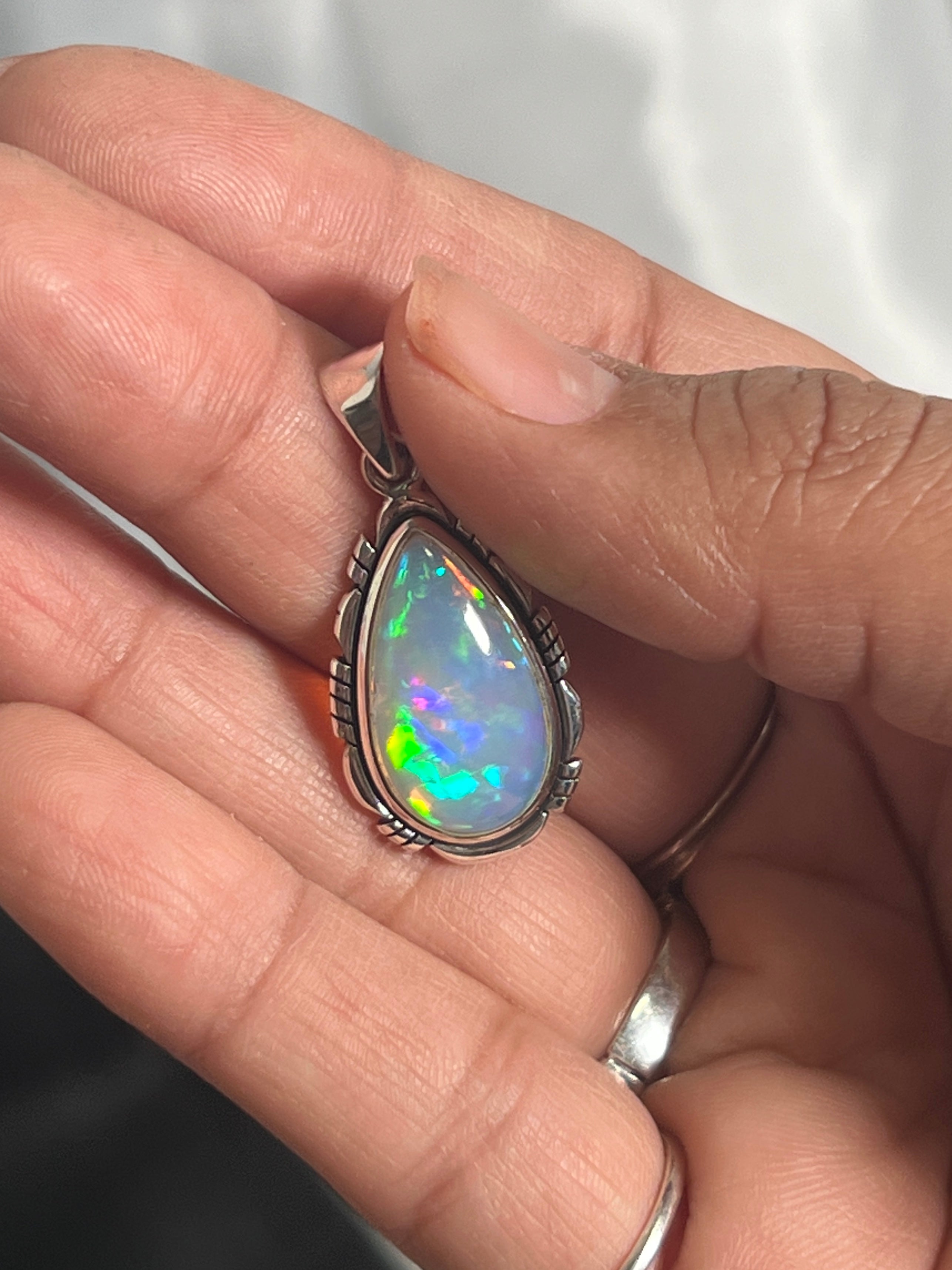 A person holding a Super Silver Ethiopian Opal Teardrop Shaped Pendant with Detailed Setting in their hand.