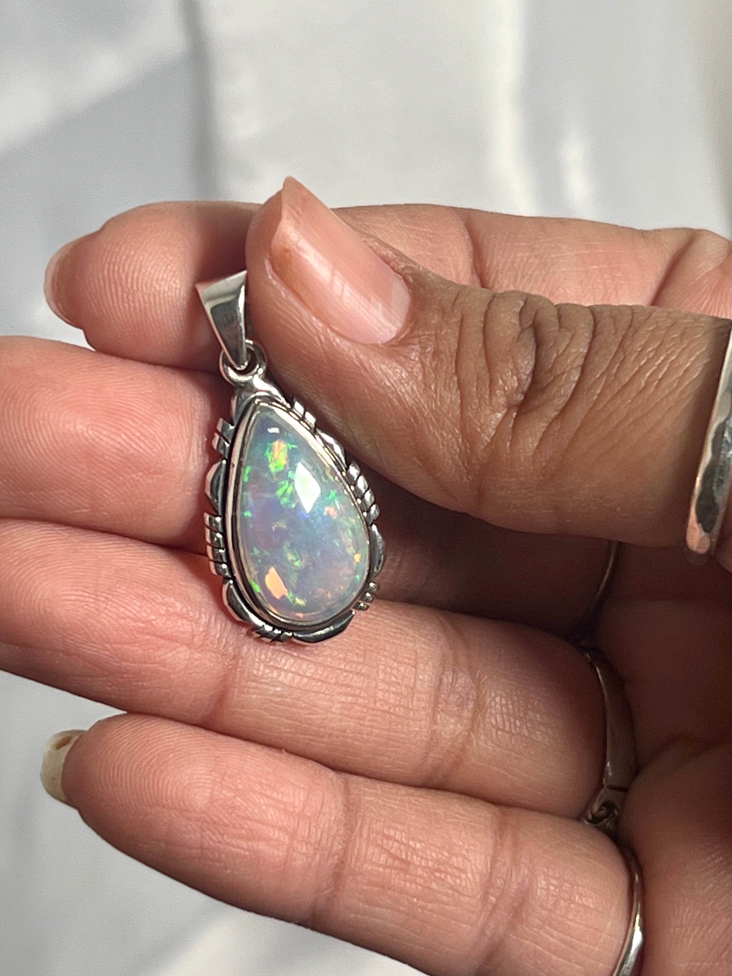 A person gracefully holding a Super Silver Ethiopian Opal Teardrop Shaped Pendant with Detailed Setting, accentuating its brilliance as a captivating statement piece.