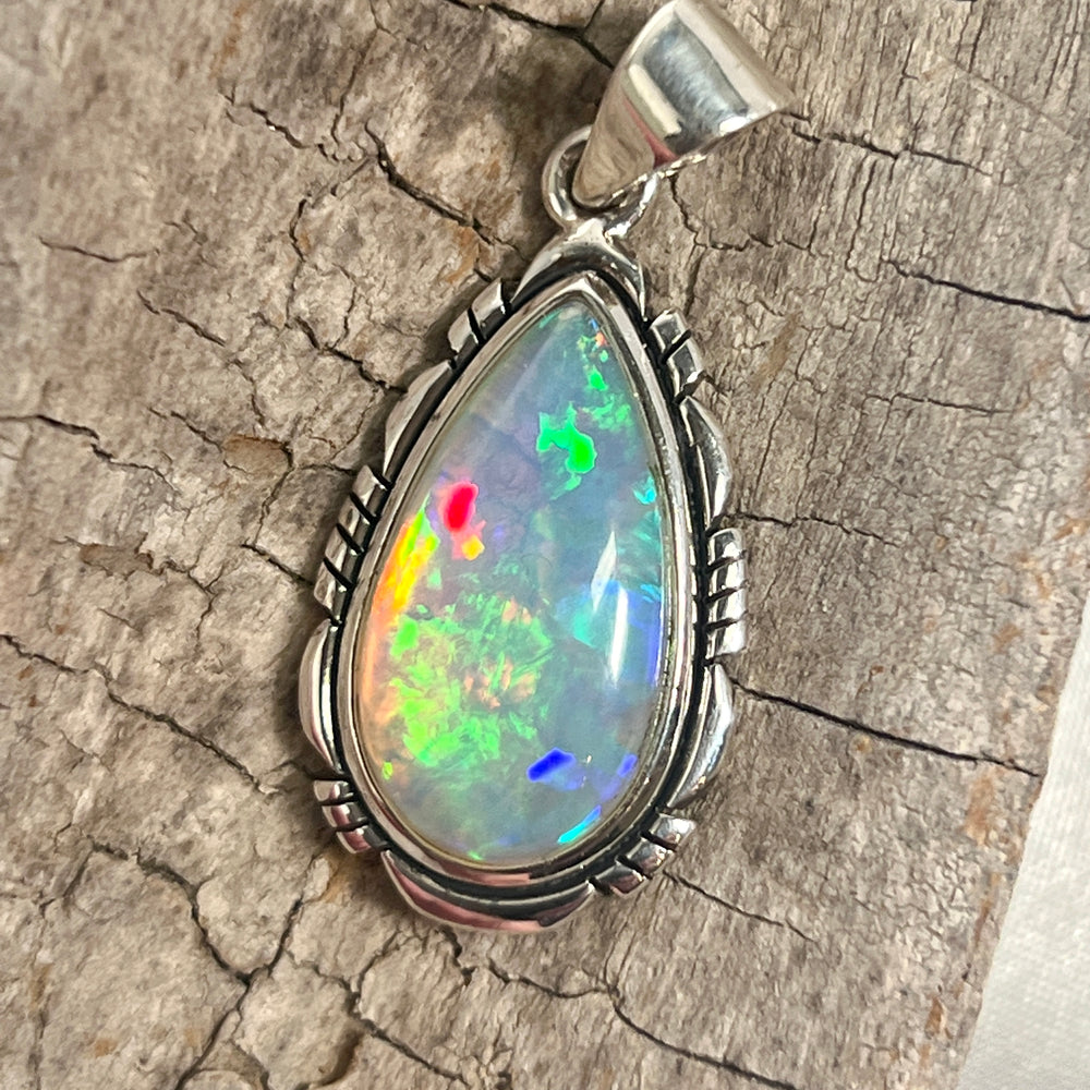 A stunning Super Silver Ethiopian Opal Teardrop Shaped Pendant with Detailed Setting, serving as a captivating statement piece, adorning a rustic piece of wood.