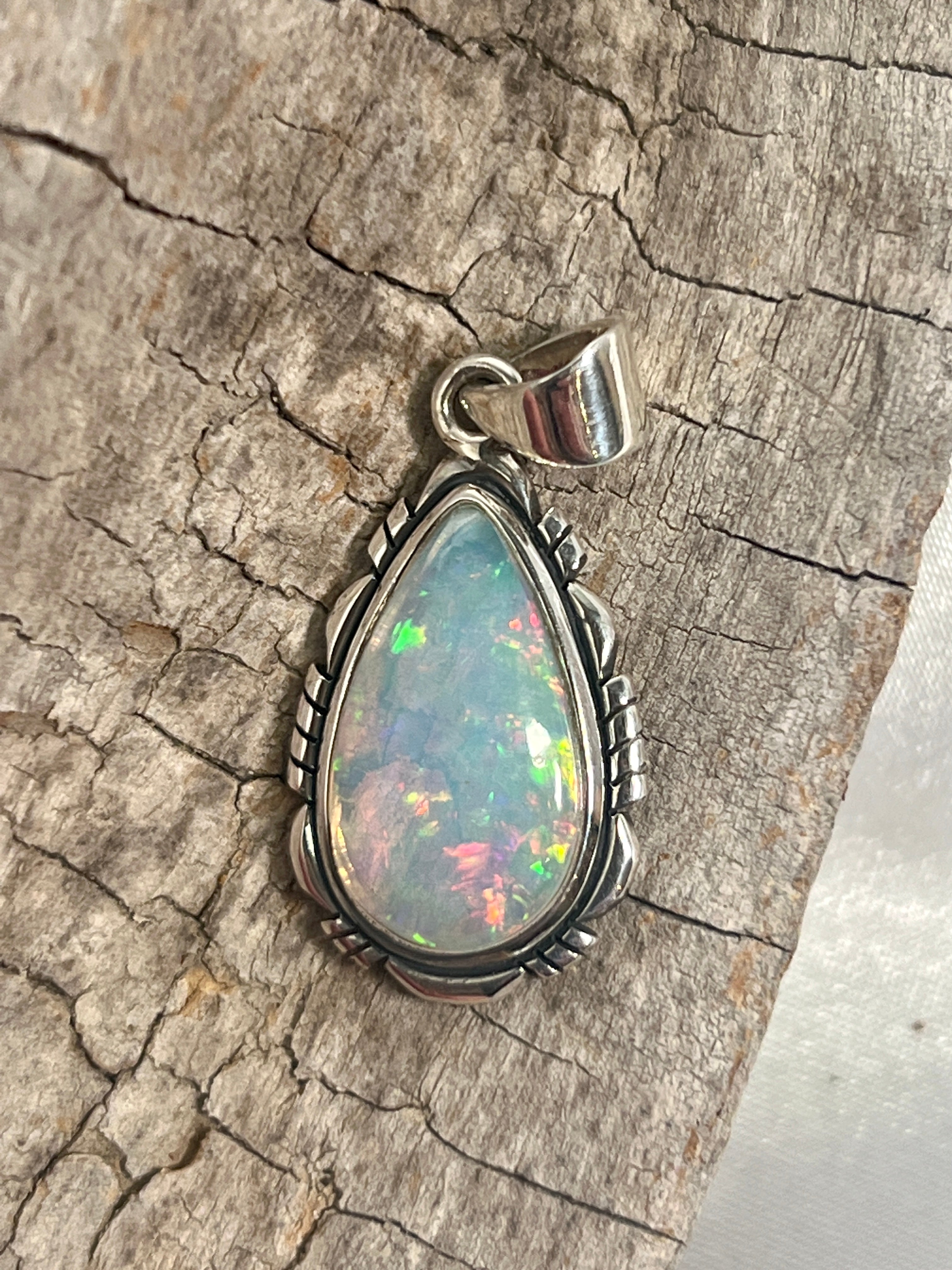 A stunning Ethiopian Opal Teardrop Shaped Pendant with Detailed Setting, truly a statement piece, delicately set on a piece of wood by Super Silver.
