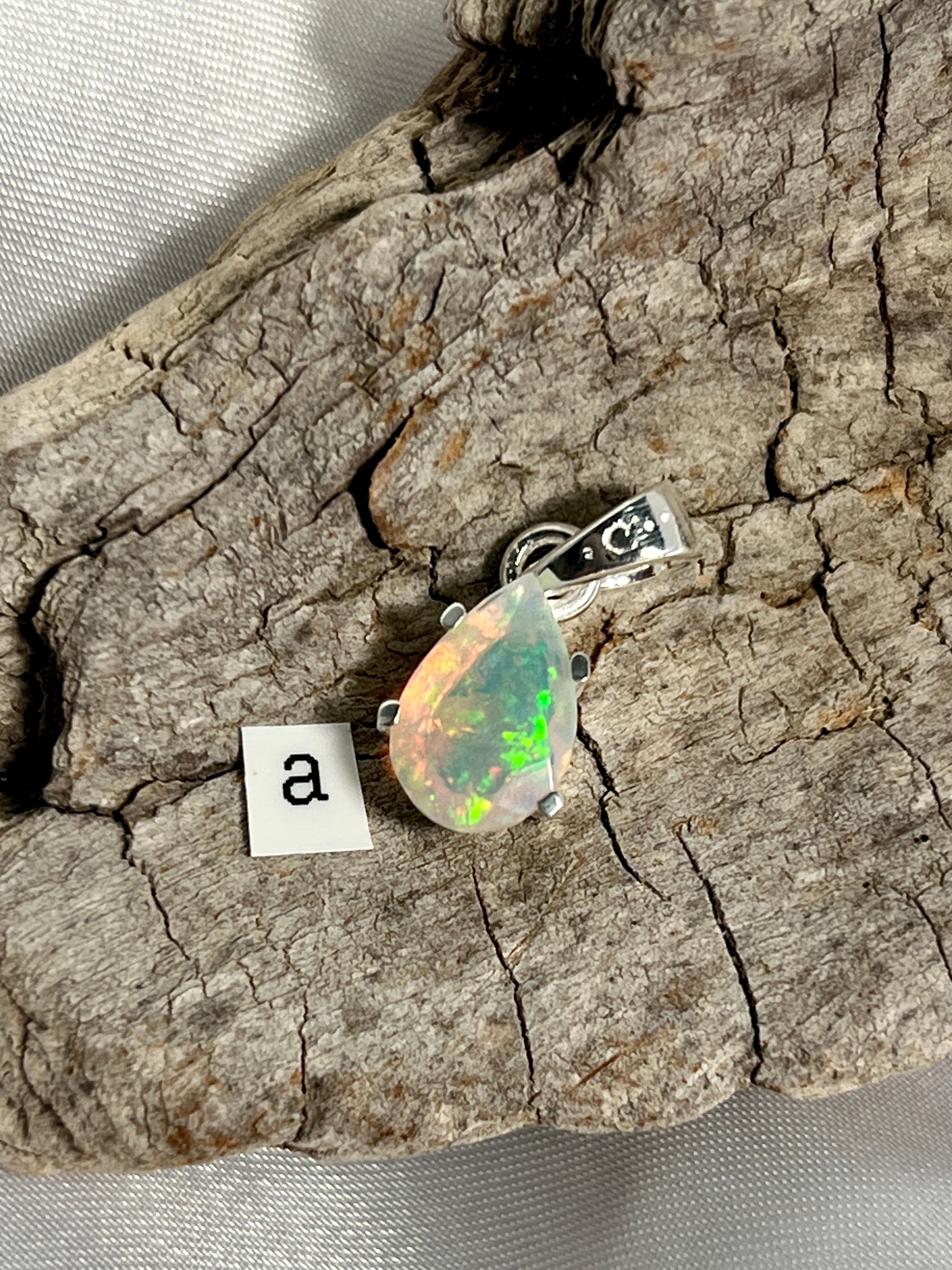 A stunning Dainty Prong Set Facet Cut Teardrop Shaped Ethiopian Opal Pendant elegantly displayed on a piece of Super Silver wood.