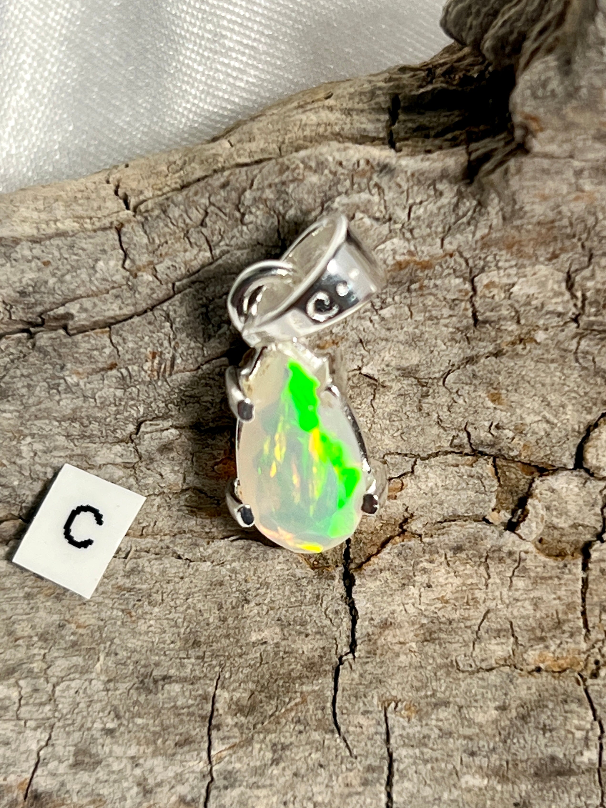 A stunning Dainty Prong Set Facet Cut Teardrop Shaped Ethiopian Opal pendant adorned with the letter "C", crafted in high-quality Sterling Silver, by Super Silver.