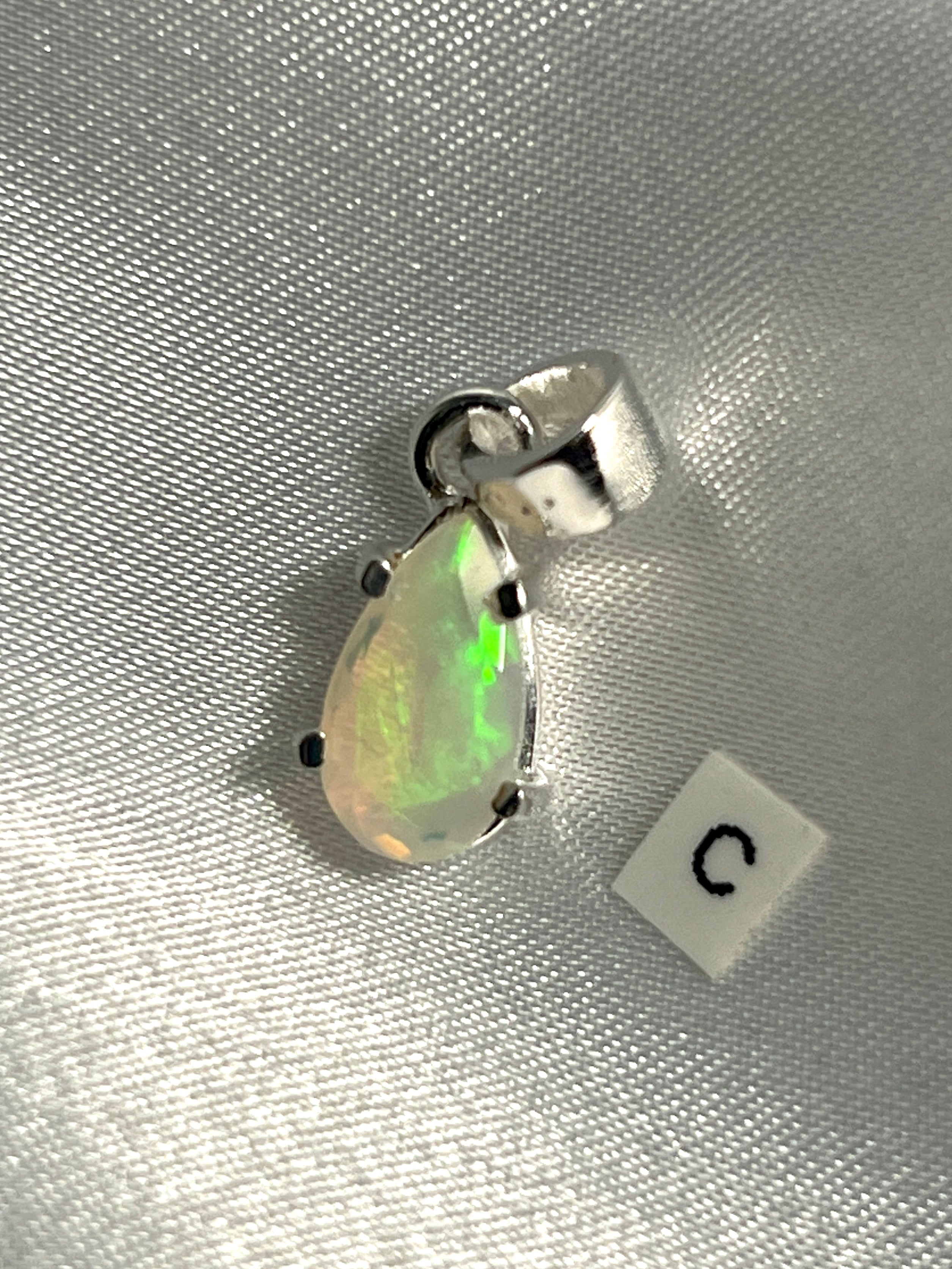 A Super Silver Dainty Prong Set Facet Cut Teardrop Shaped Ethiopian Opal Pendant with the letter c on it.