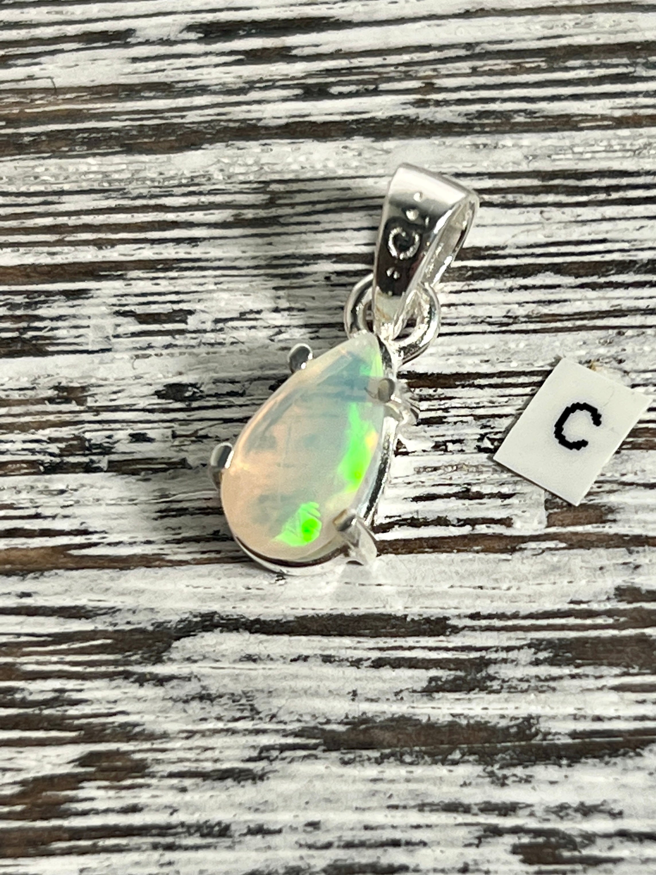 A Dainty Prong Set Facet Cut Teardrop Shaped Ethiopian Opal Pendant from Super Silver with the letter c on it.