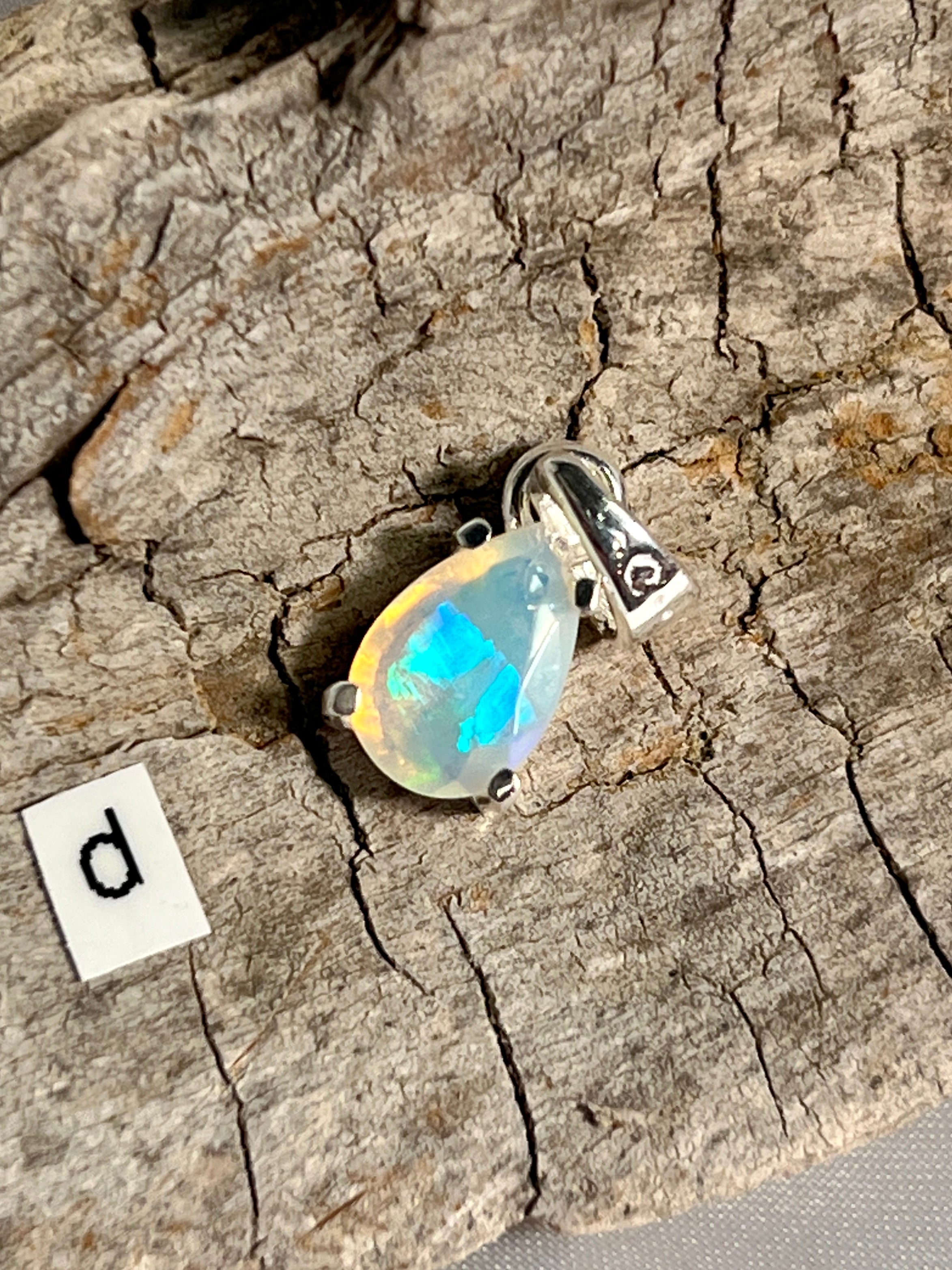 A Super Silver Dainty Prong Set Facet Cut Teardrop Shaped Ethiopian Opal Pendant on a piece of wood.