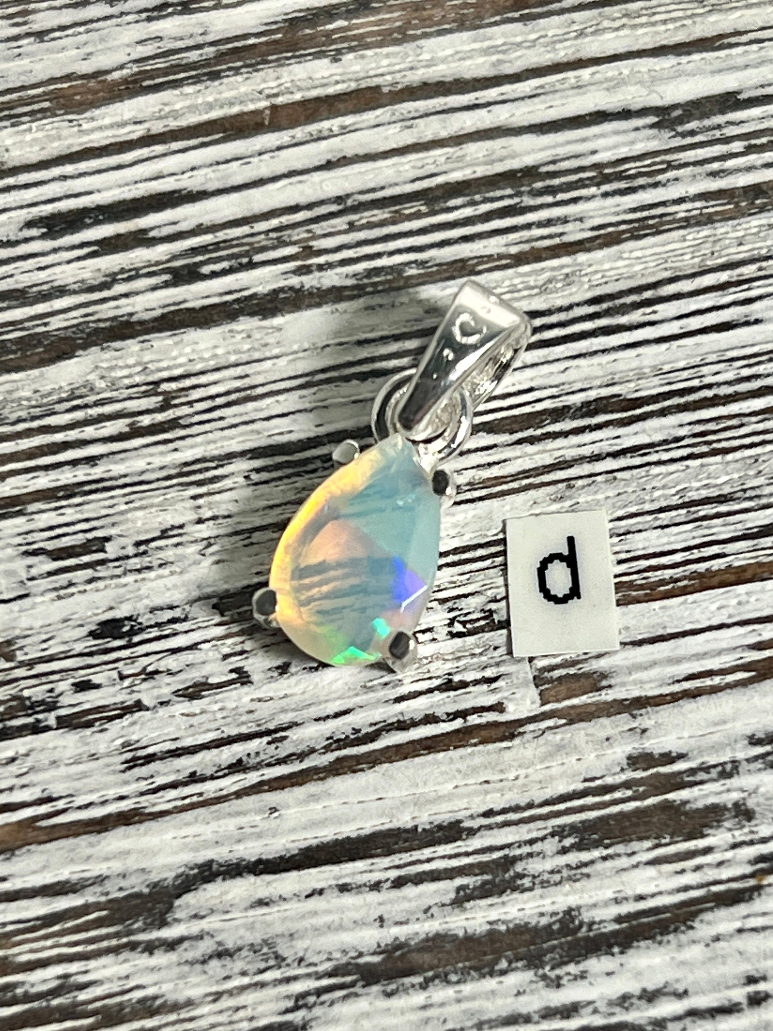 A Super Silver Dainty Prong Set Facet Cut Teardrop Shaped Ethiopian Opal Pendant adorned with a captivating Ethiopian opal and elegantly engraved with the letter d.