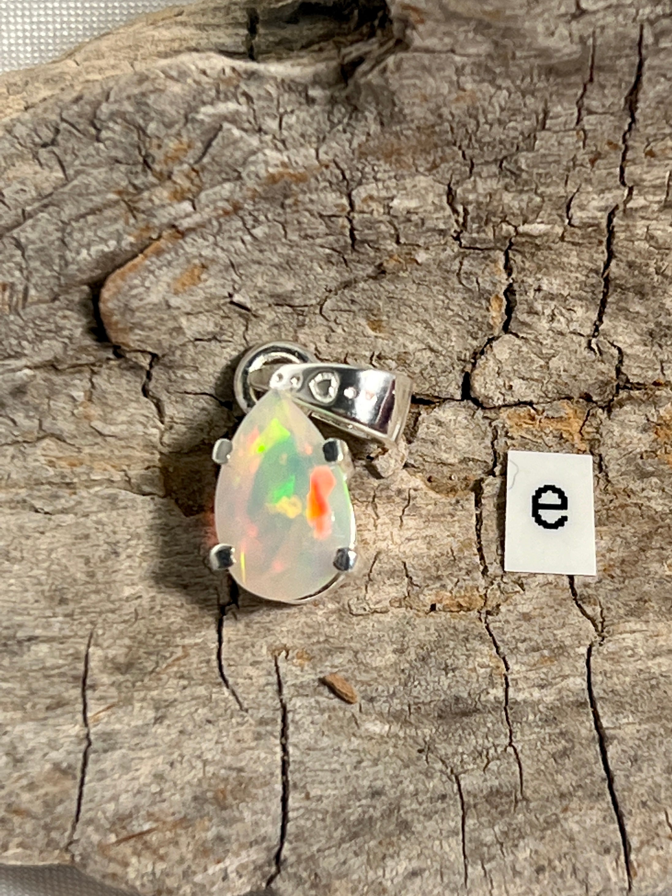 A stunning Dainty Prong Set Facet Cut Teardrop Shaped Ethiopian Opal Pendant with the letter "e" delicately engraved on it, crafted in elegant sterling silver by Super Silver.
