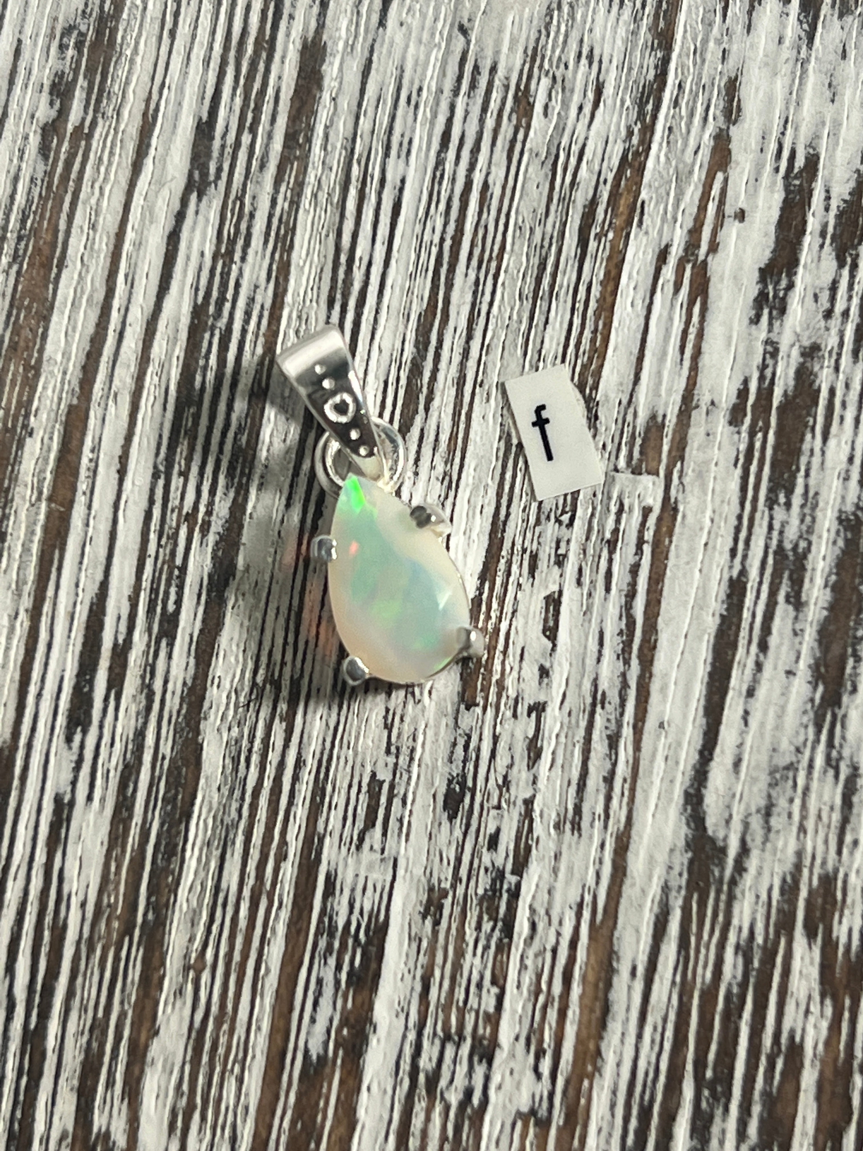 A Dainty Prong Set Facet Cut Teardrop Shaped Ethiopian Opal pendant by Super Silver on a wooden table.