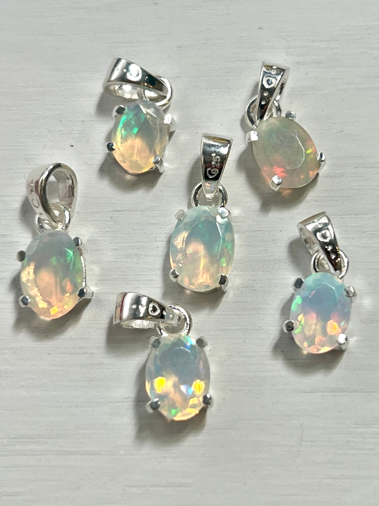 Six Tiny Facet Cut Prong Set Ethiopian Opal Pendants on a dainty, .925 Super Silver surface.