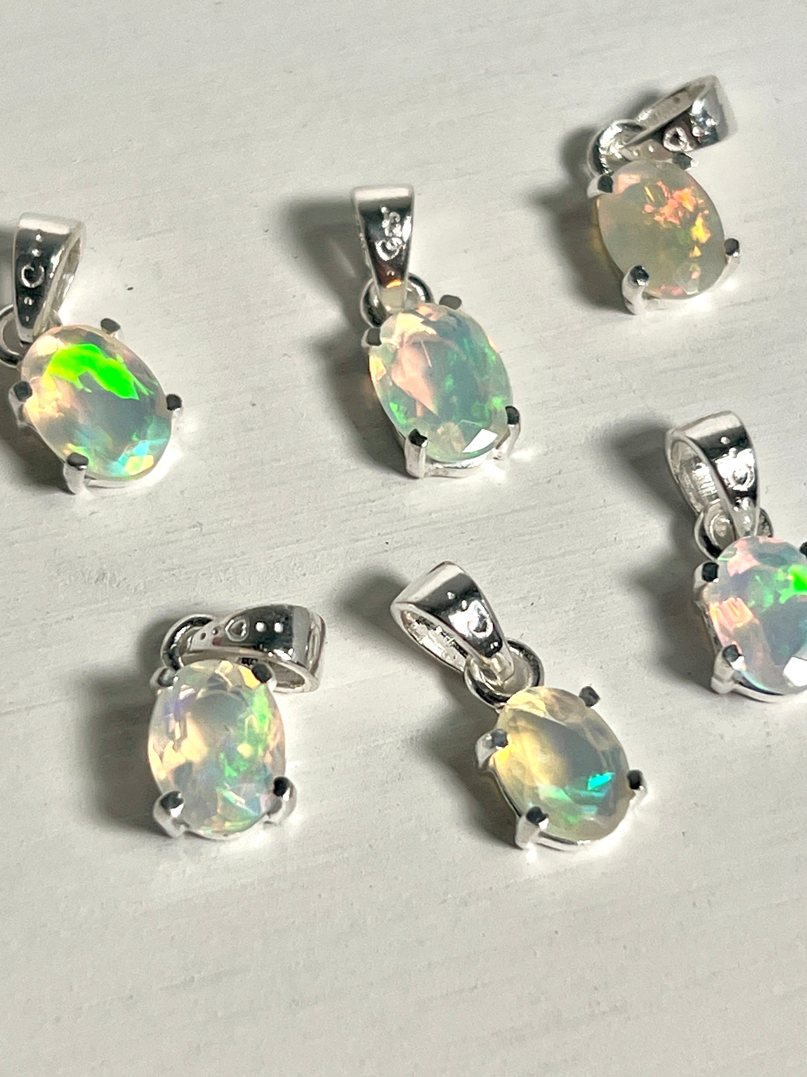 Five Tiny Facet Cut Prong Set Ethiopian Opal Pendants displayed on a white table by Super Silver.