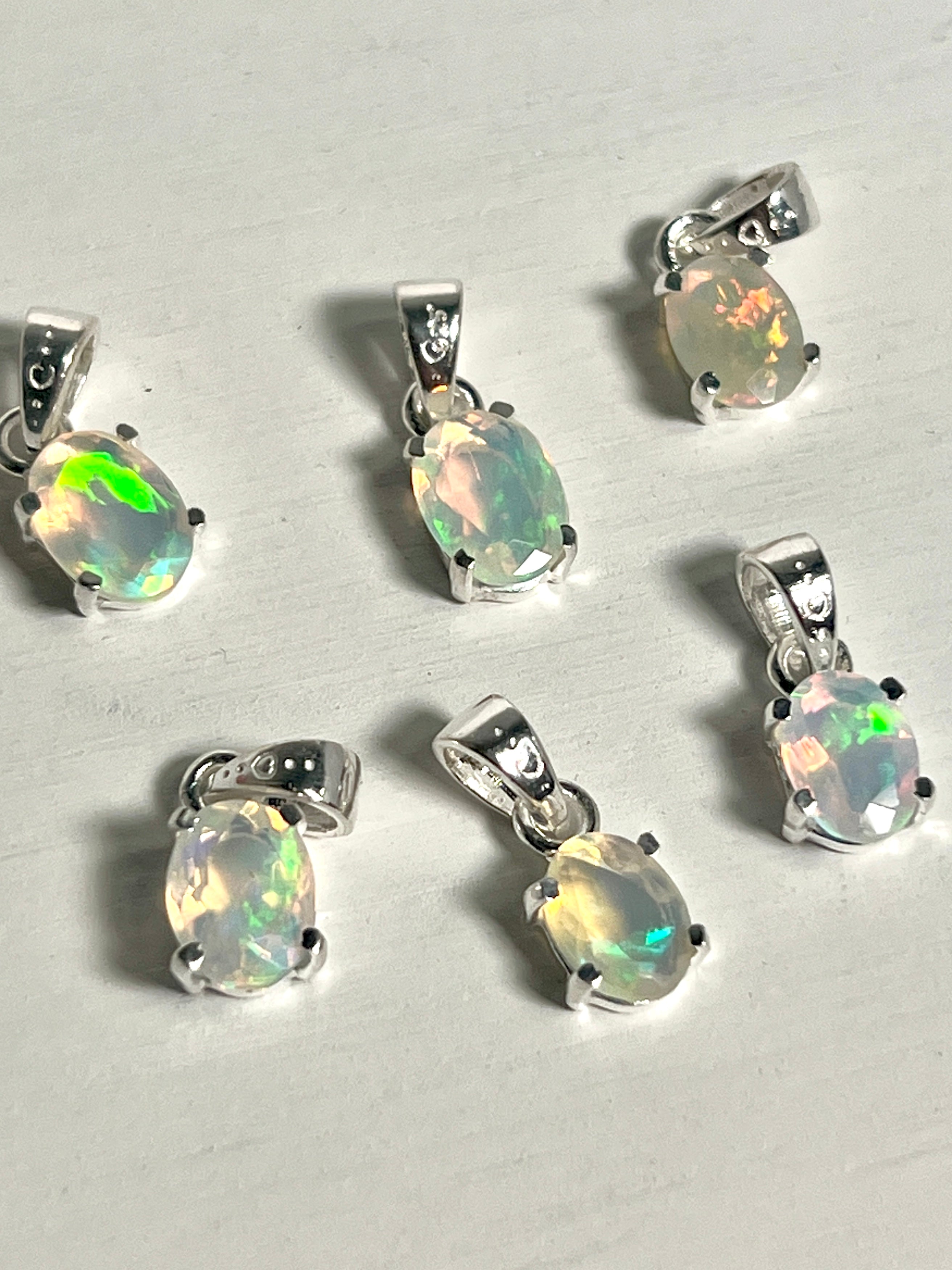 Six Super Silver Tiny Facet Cut Prong Set Ethiopian Opal Pendants on a dainty white table.