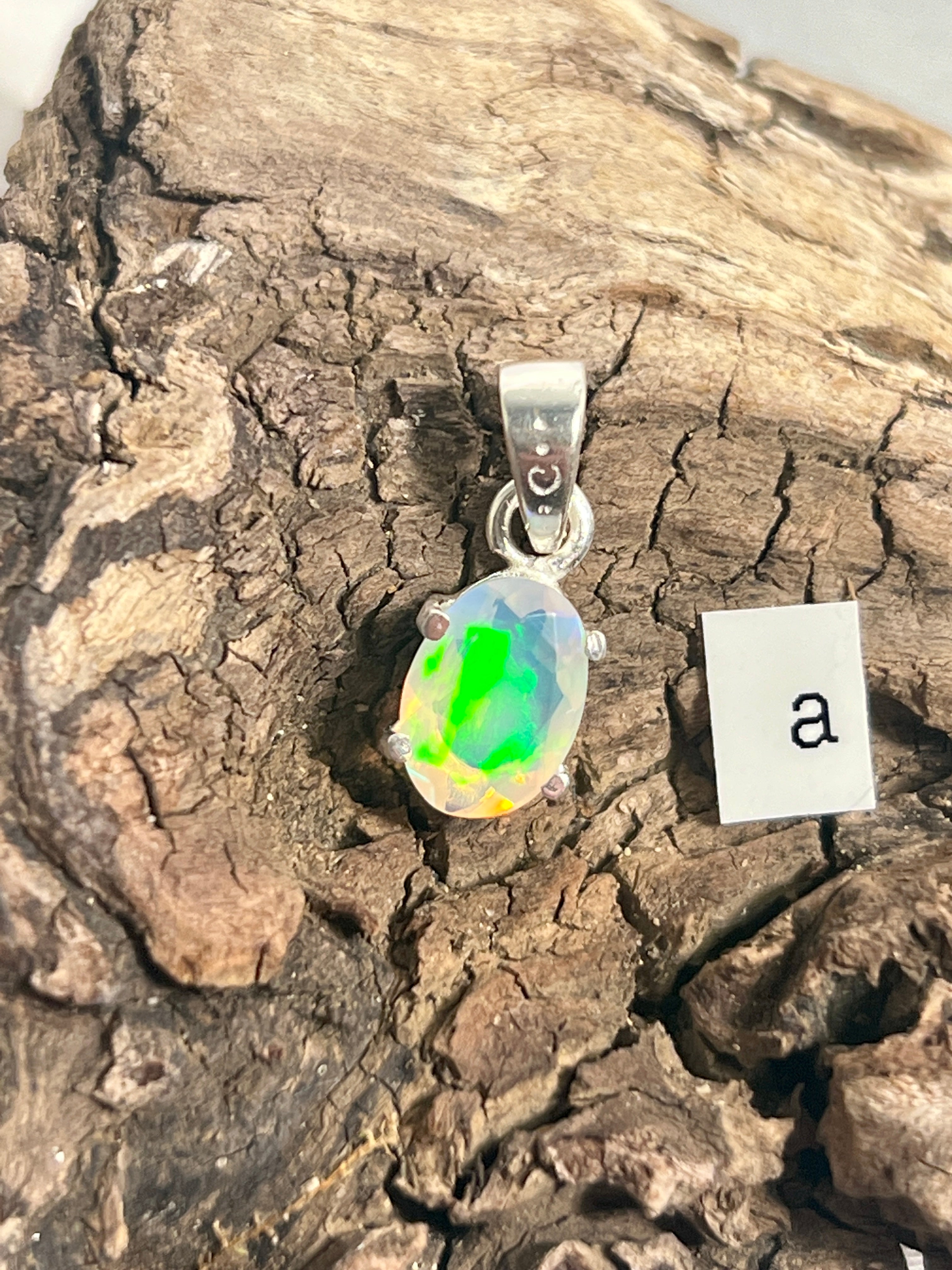 A Tiny Facet Cut Prong Set Ethiopian Opal Pendant by Super Silver on a piece of wood.