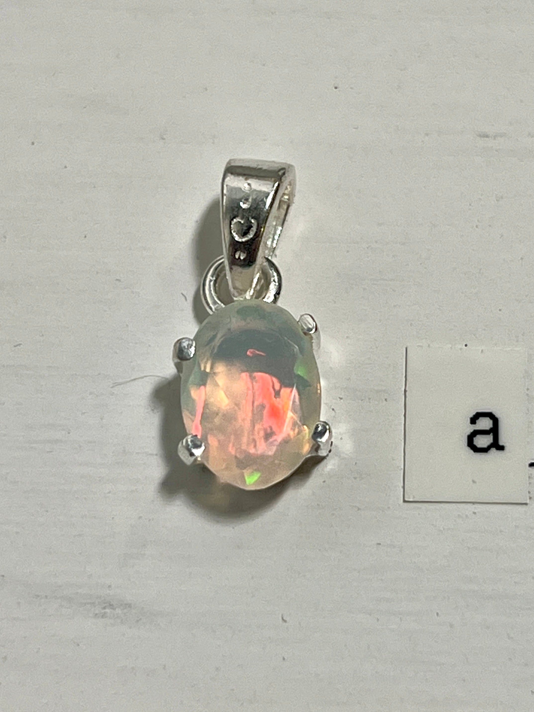 A dainty Super Silver Tiny Facet Cut Prong Set Ethiopian Opal Pendant with the letter a on it.