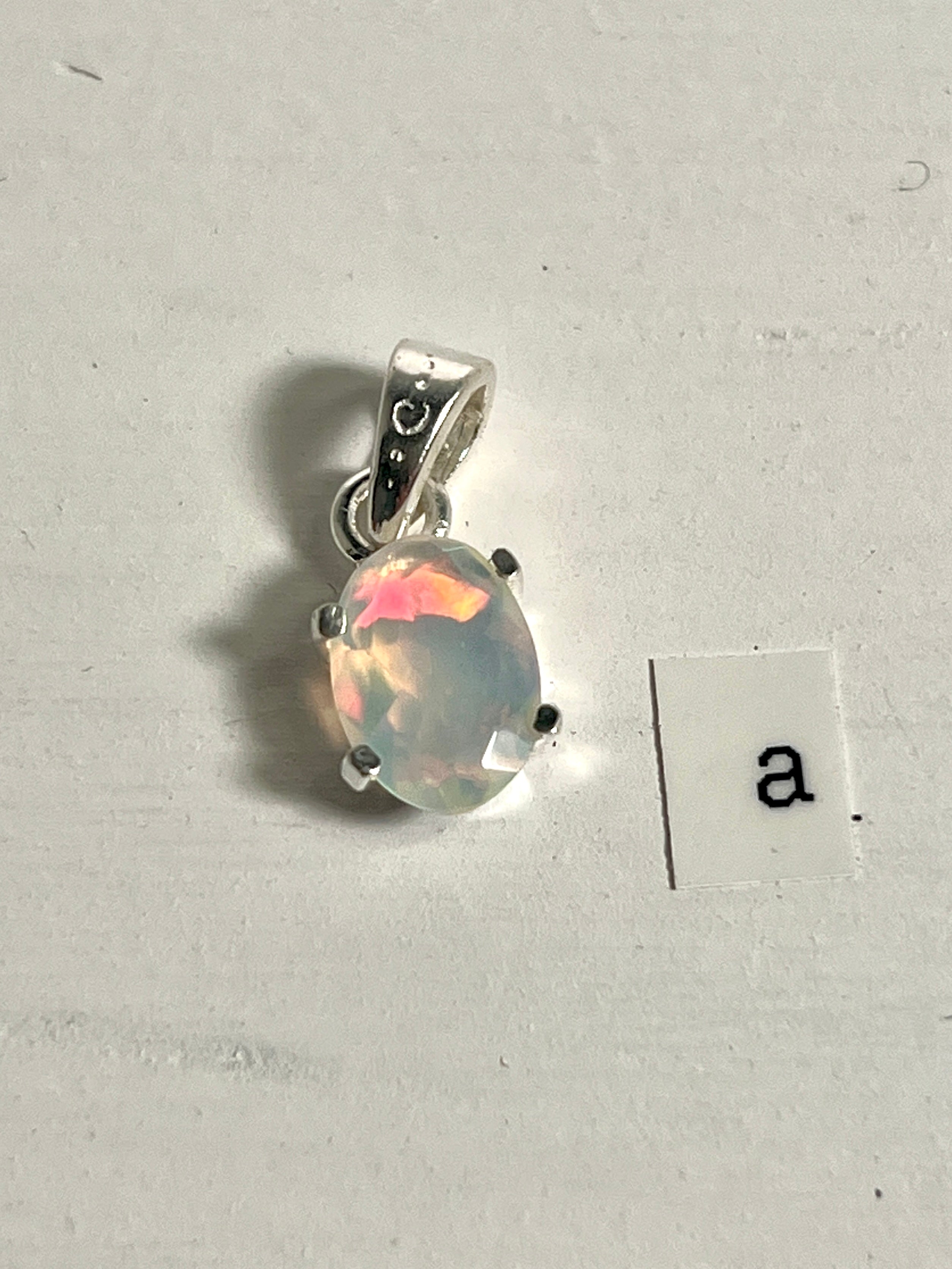 A tiny facet cut prong set Ethiopian Opal pendant with the letter a next to it, crafted in .925 sterling silver by Super Silver.