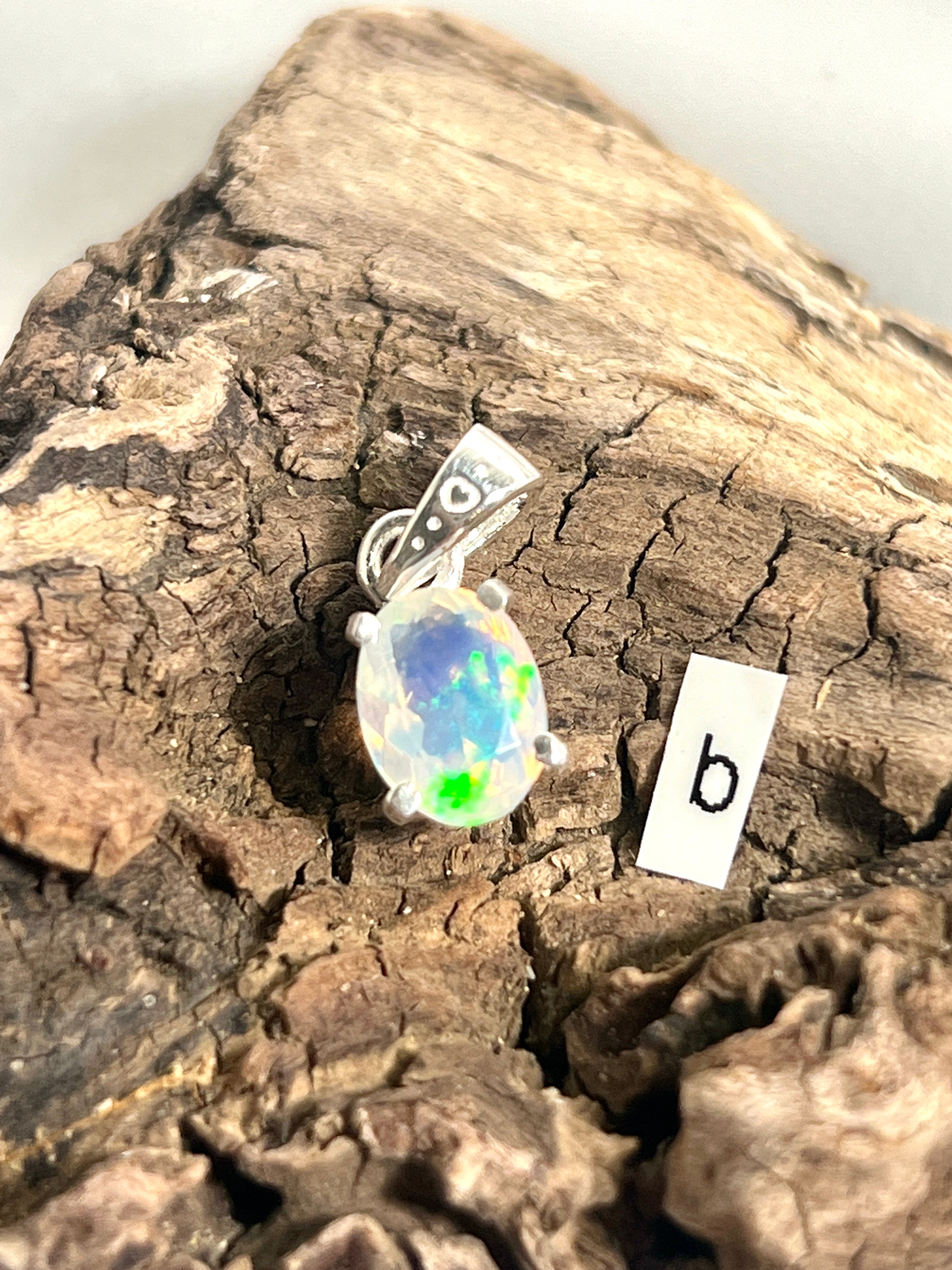 A dainty Super Silver Tiny Facet Cut Prong Set Ethiopian Opal Pendant with the letter b on it.