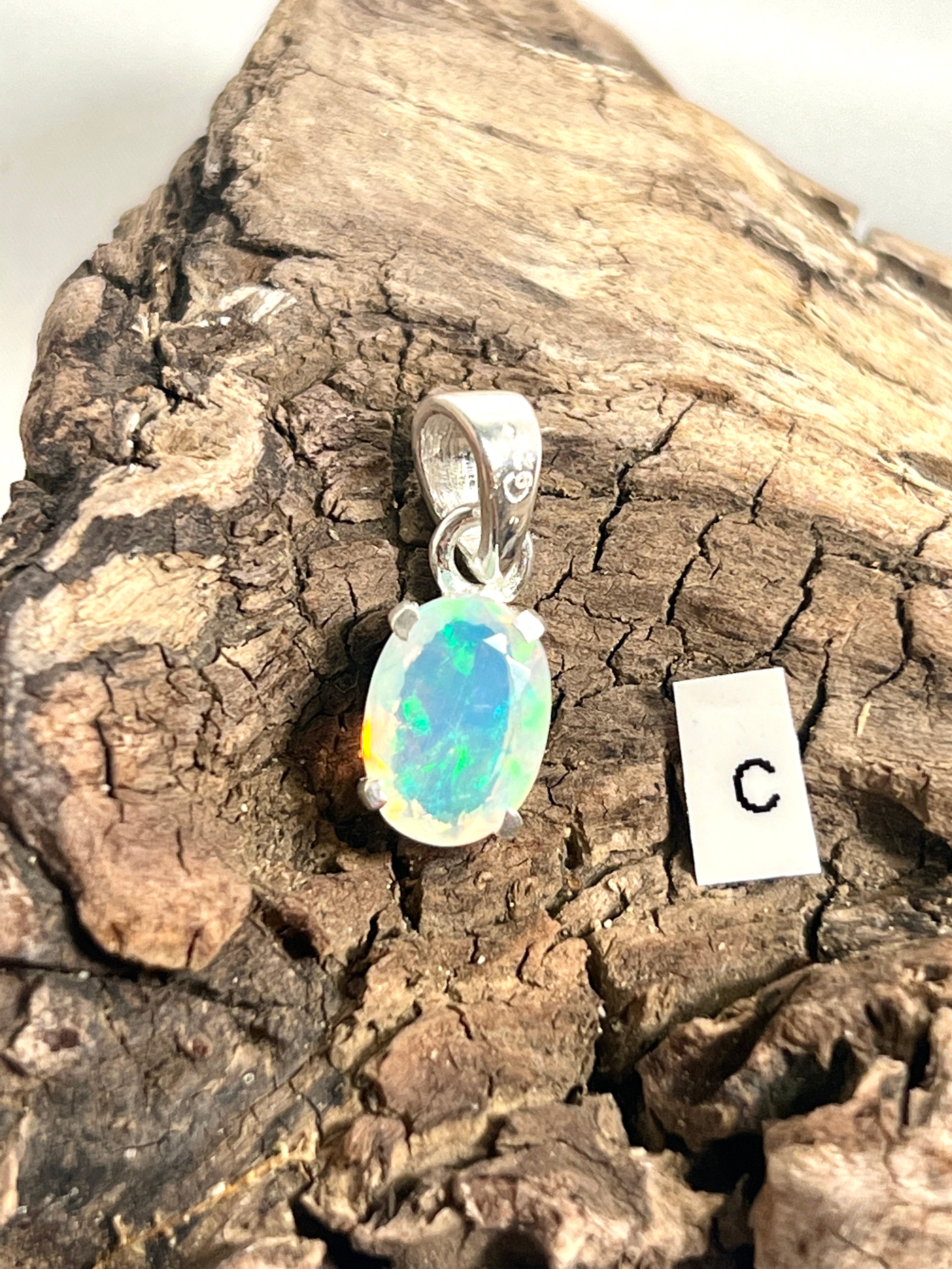 A dainty pendant crafted from .925 sterling silver, featuring an Ethiopian opal with the letter c elegantly engraved on it, called the Tiny Facet Cut Prong Set Ethiopian Opal Pendant by Super Silver.