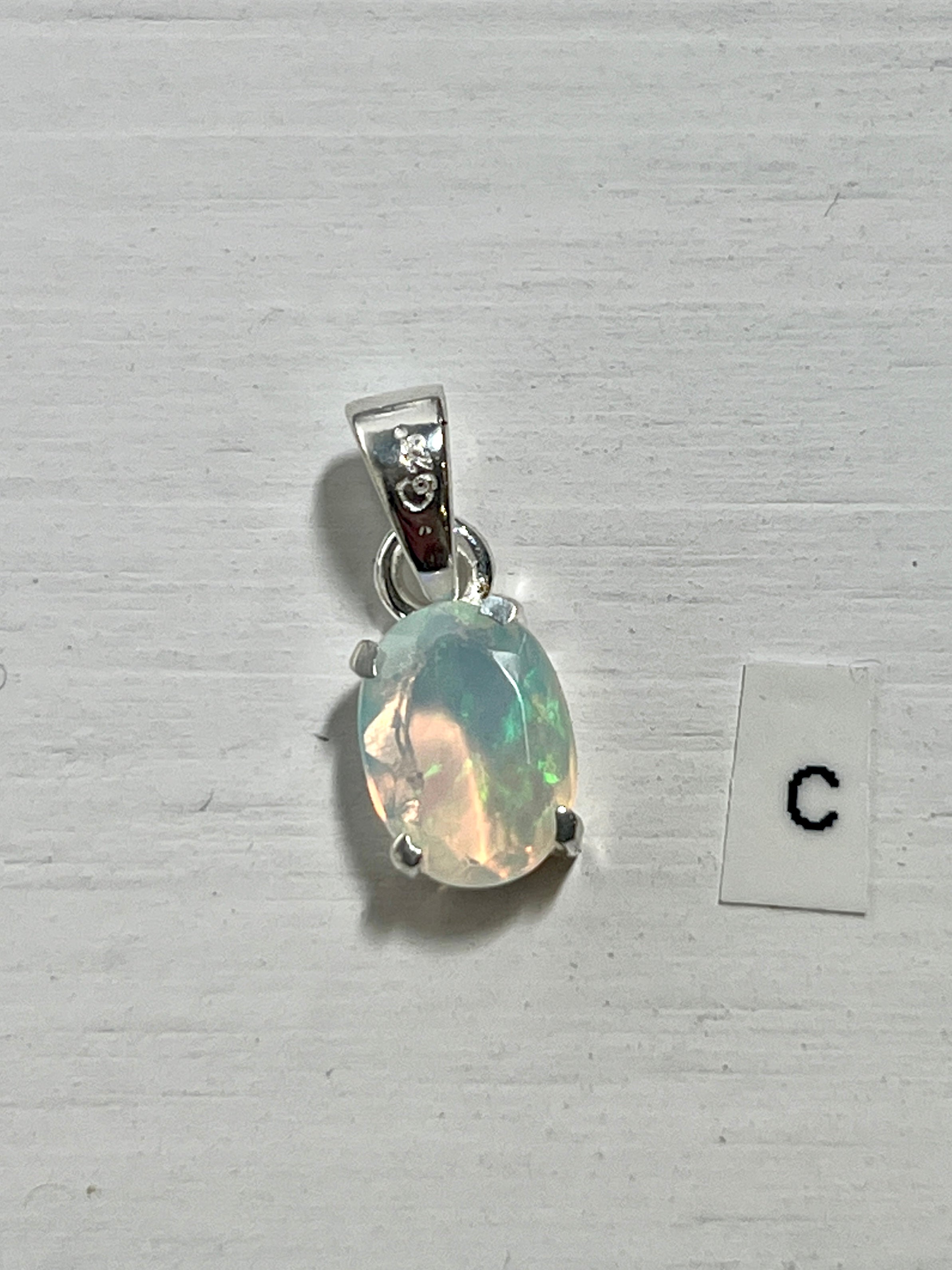 A dainty Super Silver Tiny Facet Cut Prong Set Ethiopian Opal Pendant with the letter c next to it, made of .925 sterling silver.