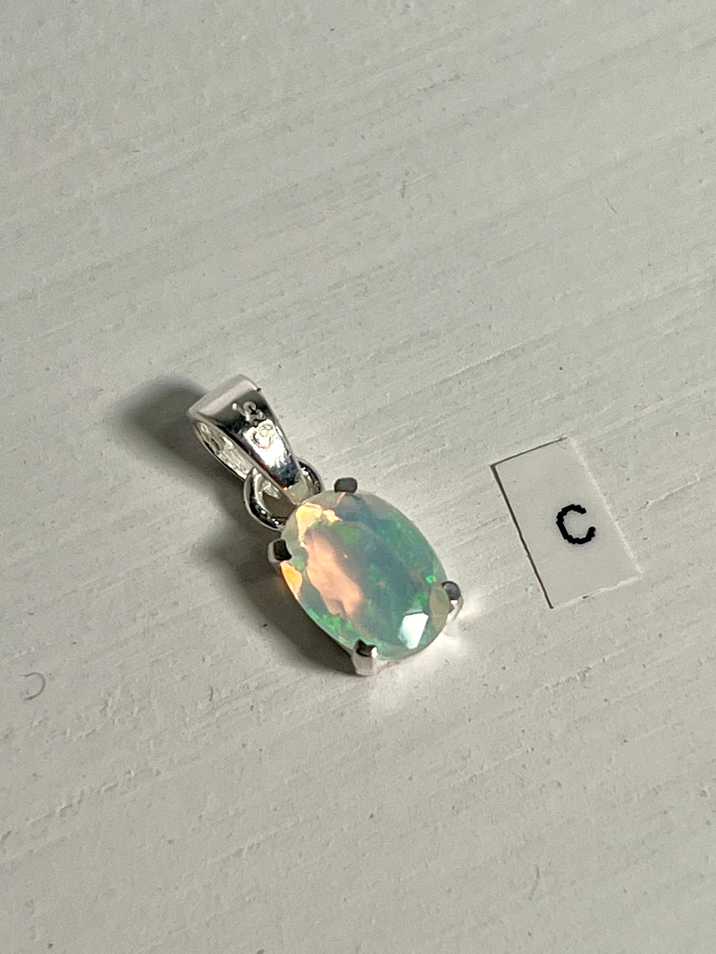 A dainty pendant made by Super Silver, featuring a Tiny Facet Cut Prong Set Ethiopian Opal and the letter c.
