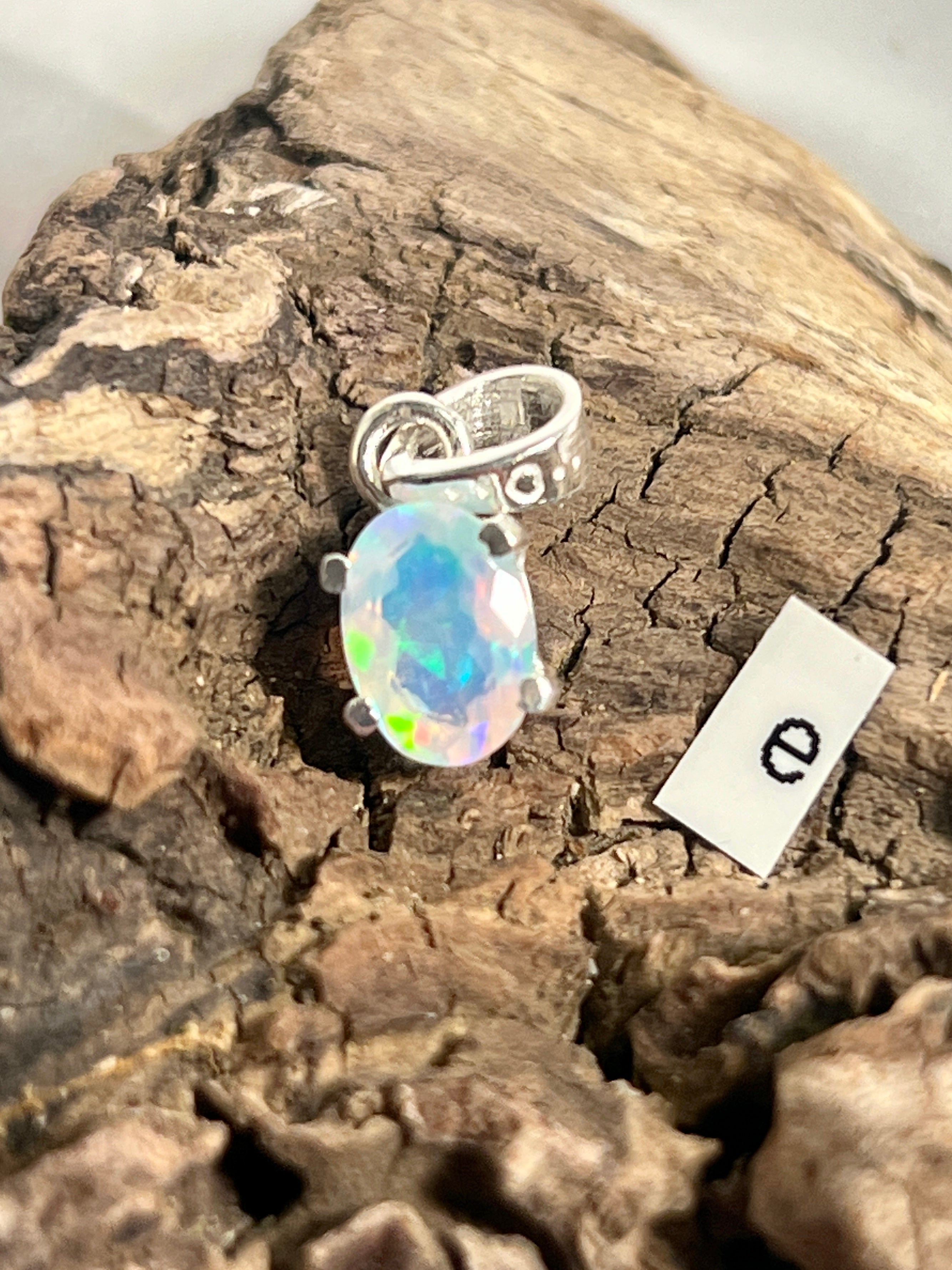 A Tiny Facet Cut Prong Set Ethiopian Opal Pendant by Super Silver on a piece of wood.