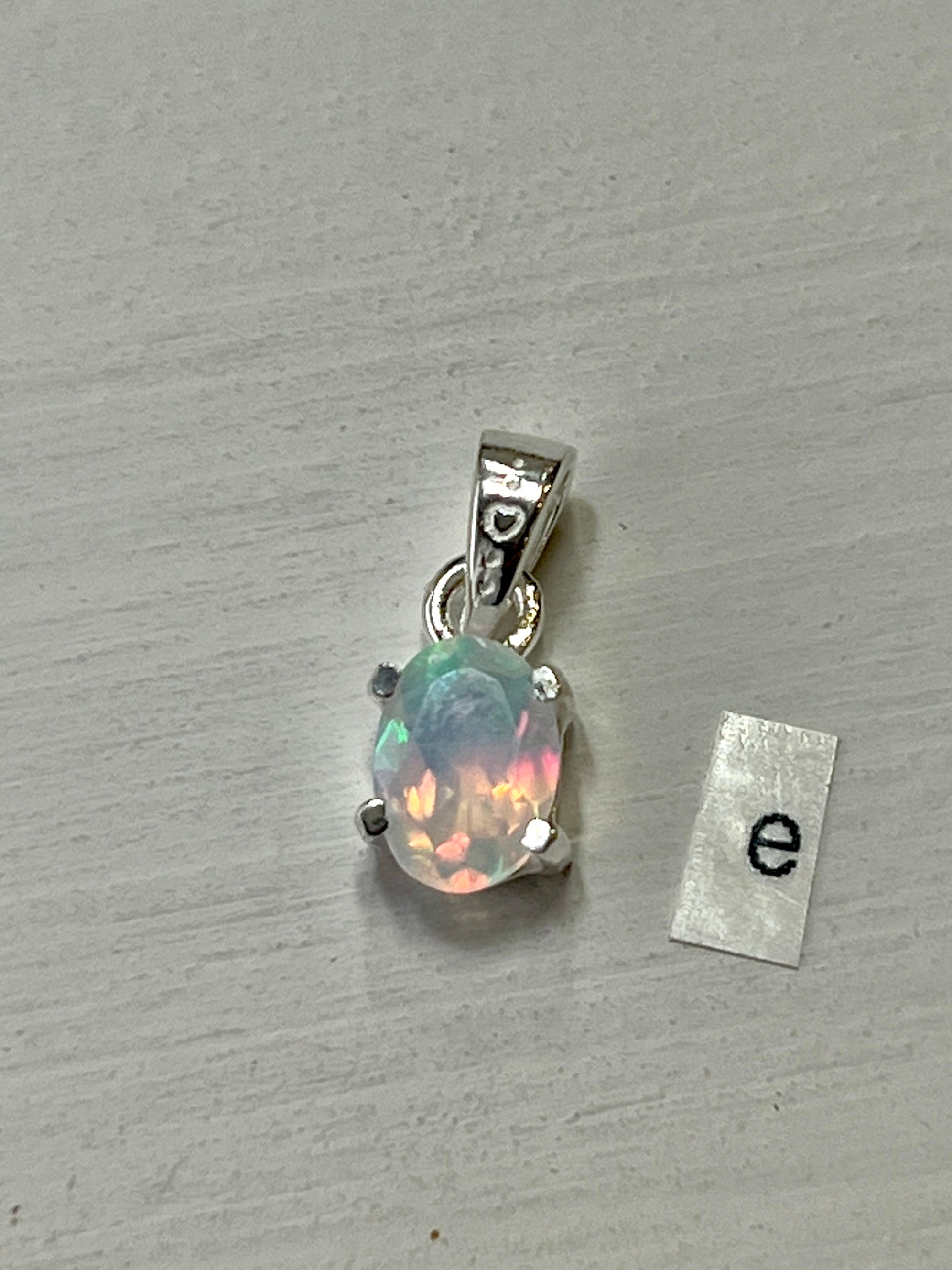A Tiny Facet Cut Prong Set Ethiopian Opal Pendant featuring an Ethiopian opal and crafted by Super Silver in .925 sterling silver, adorned with the letter e.