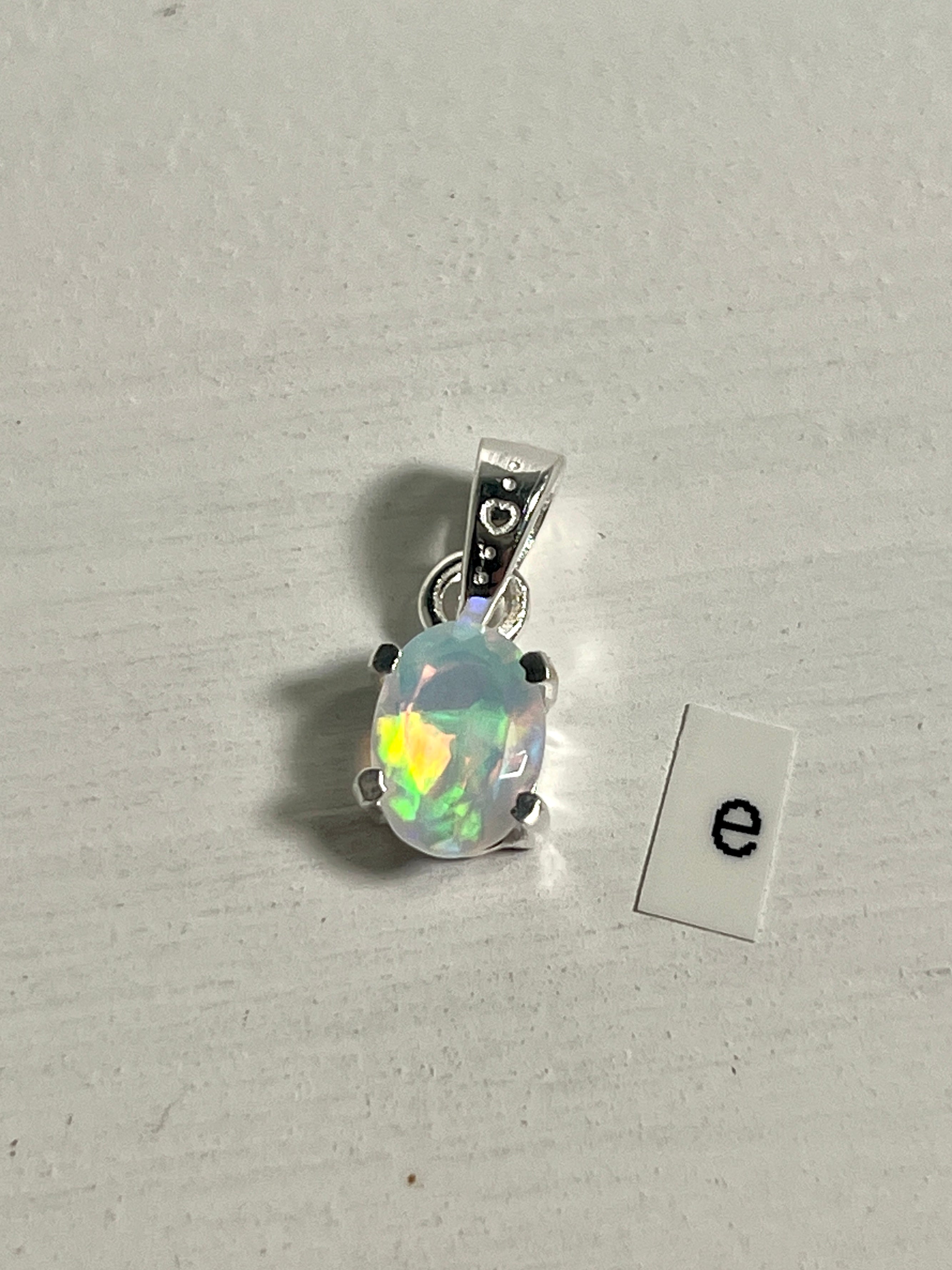 A dainty Tiny Facet Cut Prong Set Ethiopian Opal Pendant with the letter e, crafted in .925 sterling silver from Super Silver.