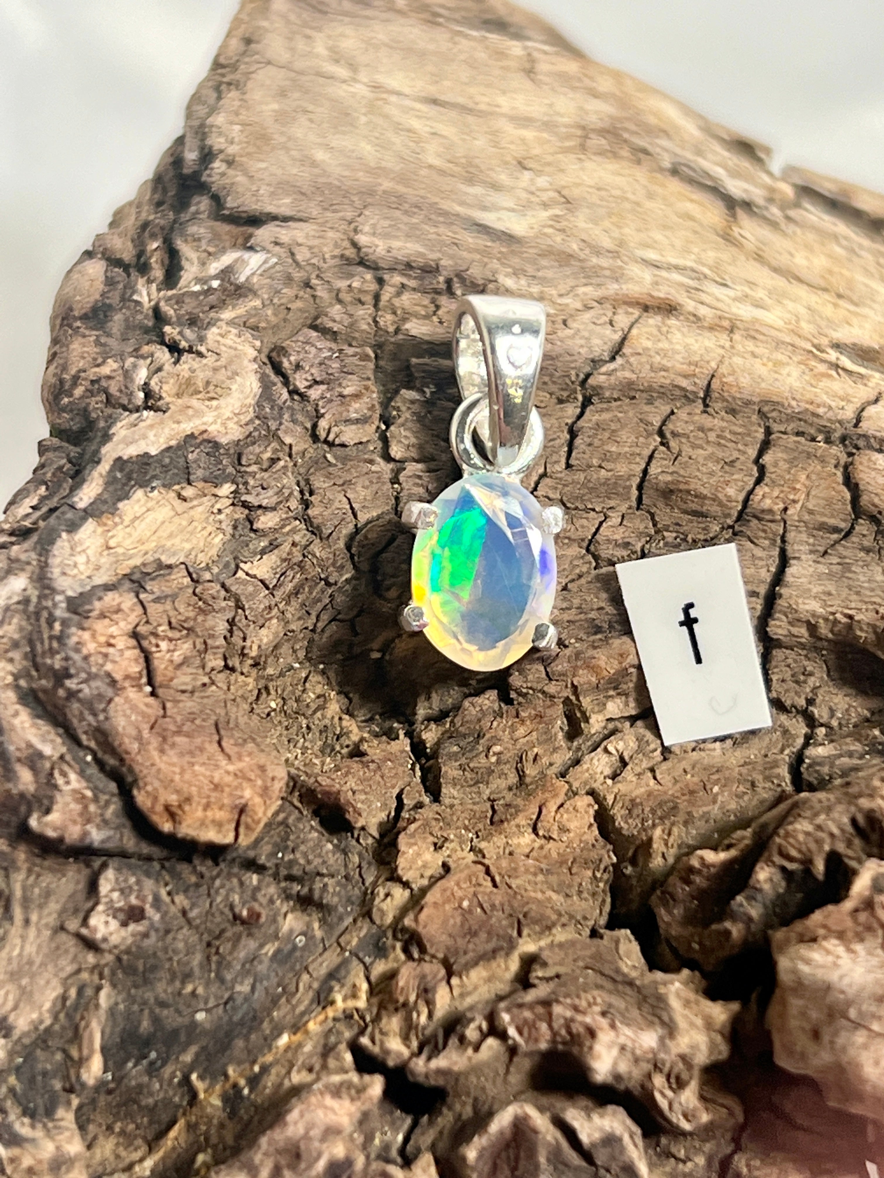 A Tiny Facet Cut Prong Set Ethiopian Opal Pendant by Super Silver on a piece of wood.