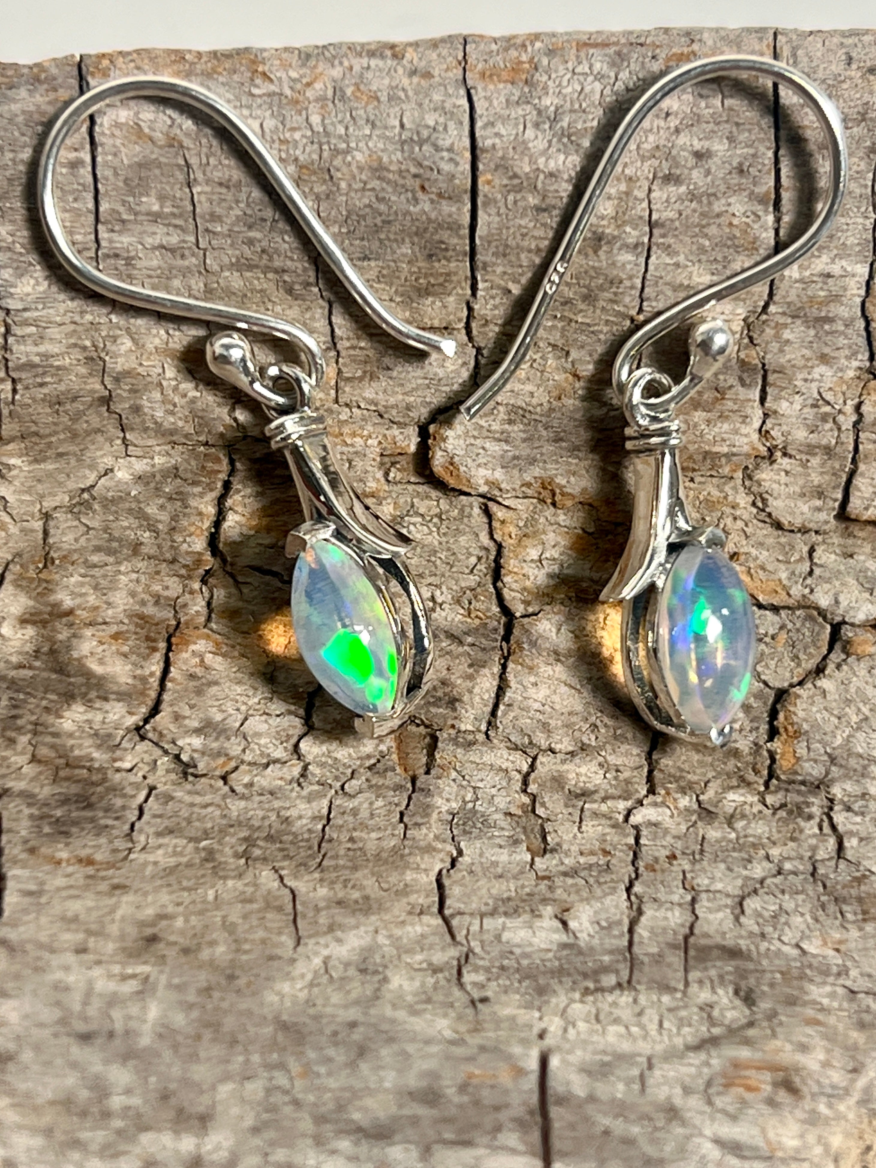 A pair of dainty Modern Marquise Shaped Ethiopian Opal Earrings by Super Silver on a piece of wood.