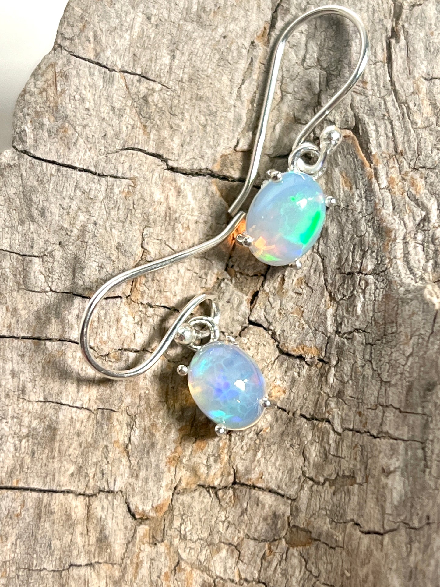 A pair of Super Silver Vibrant Oval Ethiopian Opal Earrings exuding natural brilliance on a rock, showcasing vibrant hues.