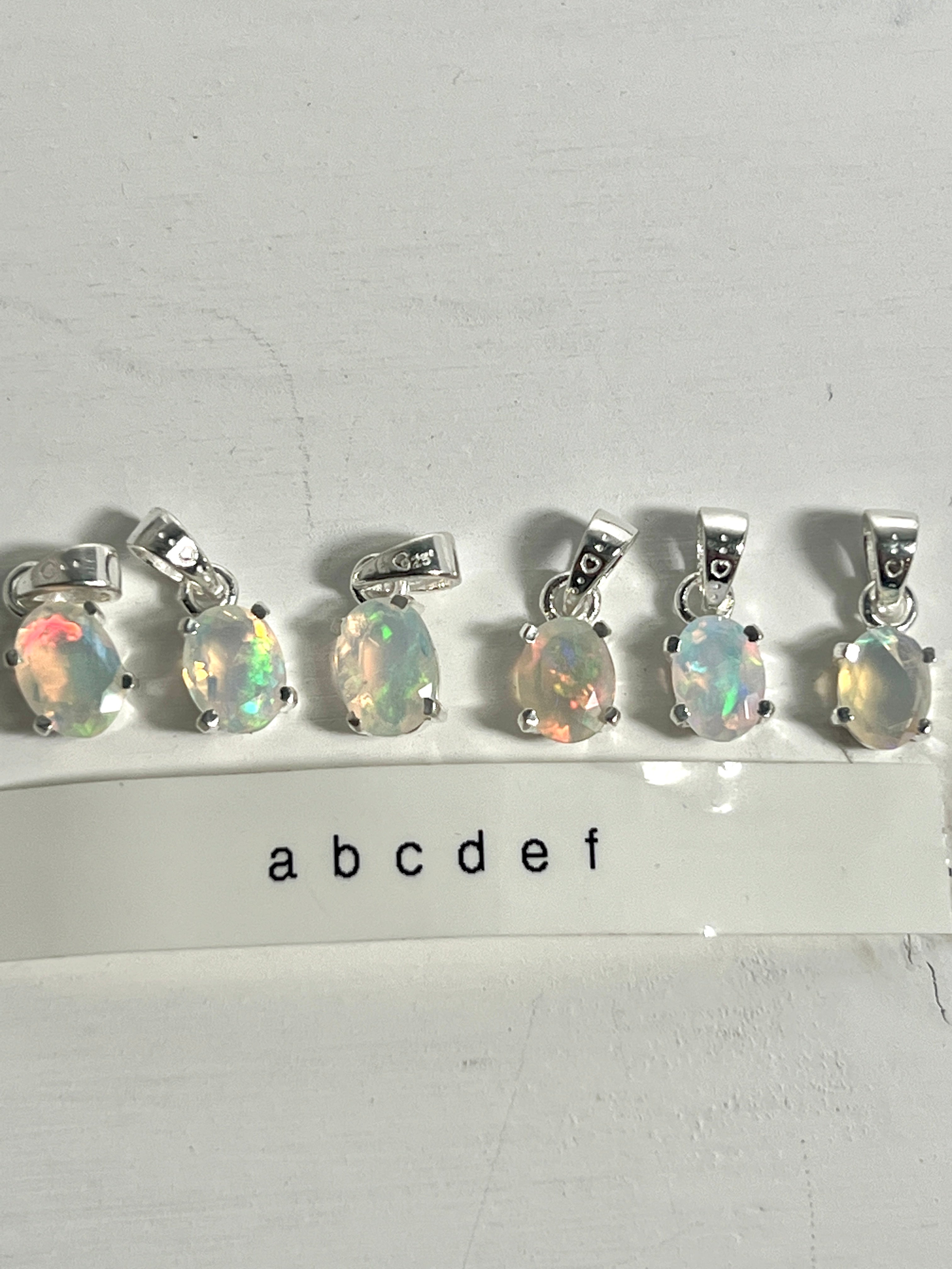 A set of dainty Super Silver Tiny Facet Cut Prong Set Ethiopian Opal Pendants, crafted in .925 sterling silver, each adorned with the letter abc.