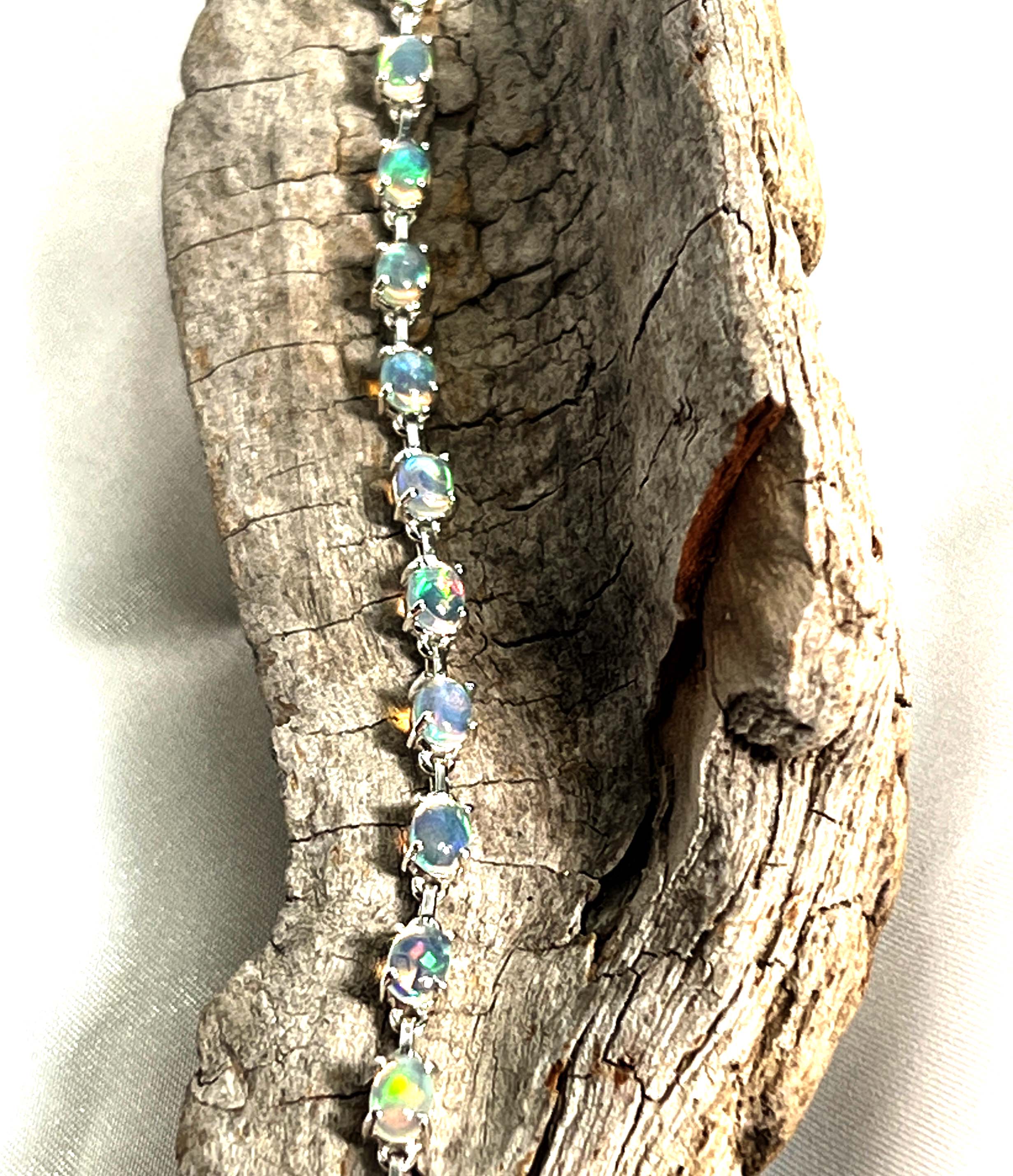 A glamorous Delicate Ethiopian Opal Bracelet adorned with opal stones on a piece of wood, by Super Silver.