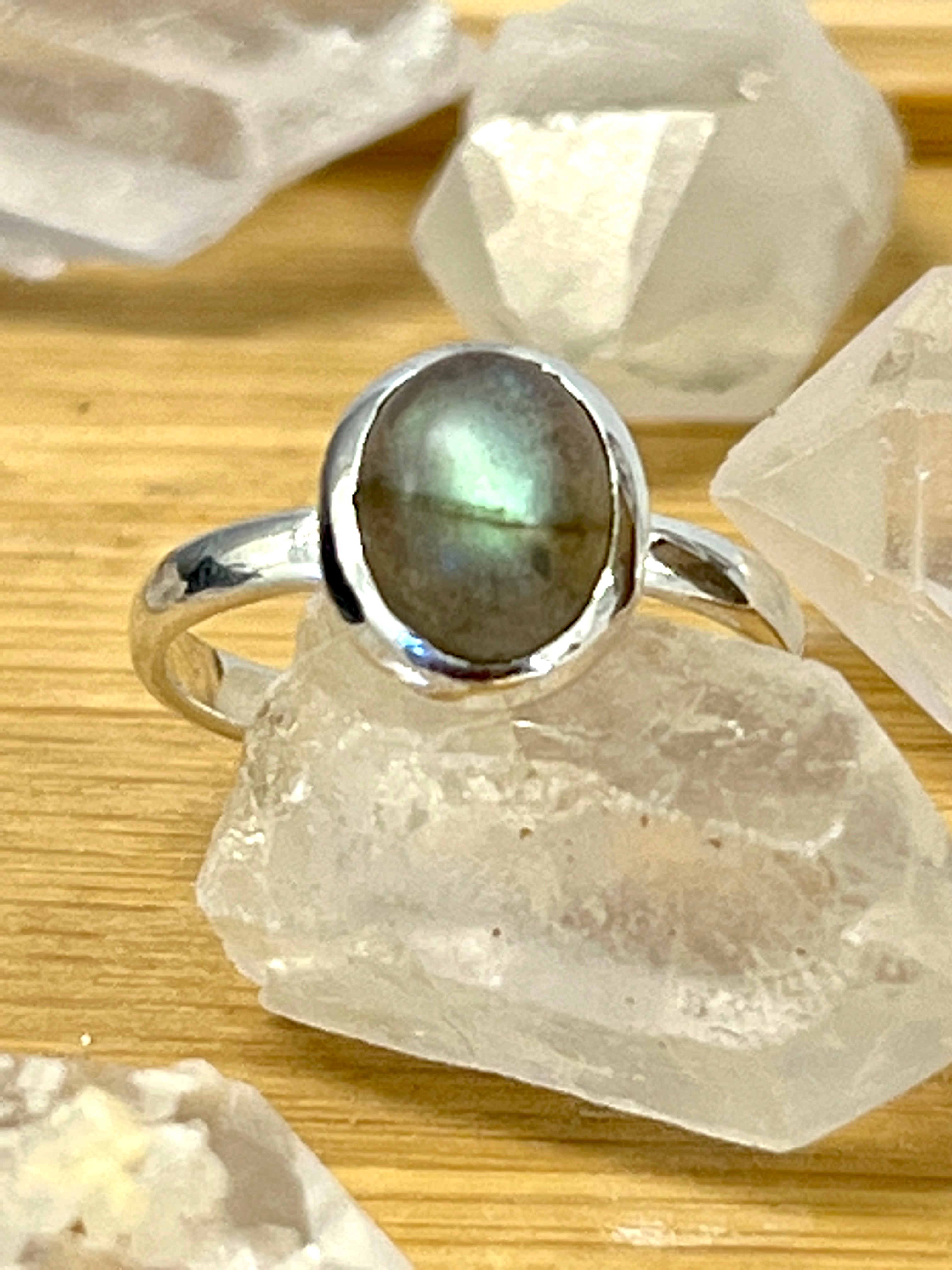 A teardrop-shaped engagement ring adorned with a mesmerizing Simple Oval Moonstone Or Labradorite Ring amidst sparkling crystals.