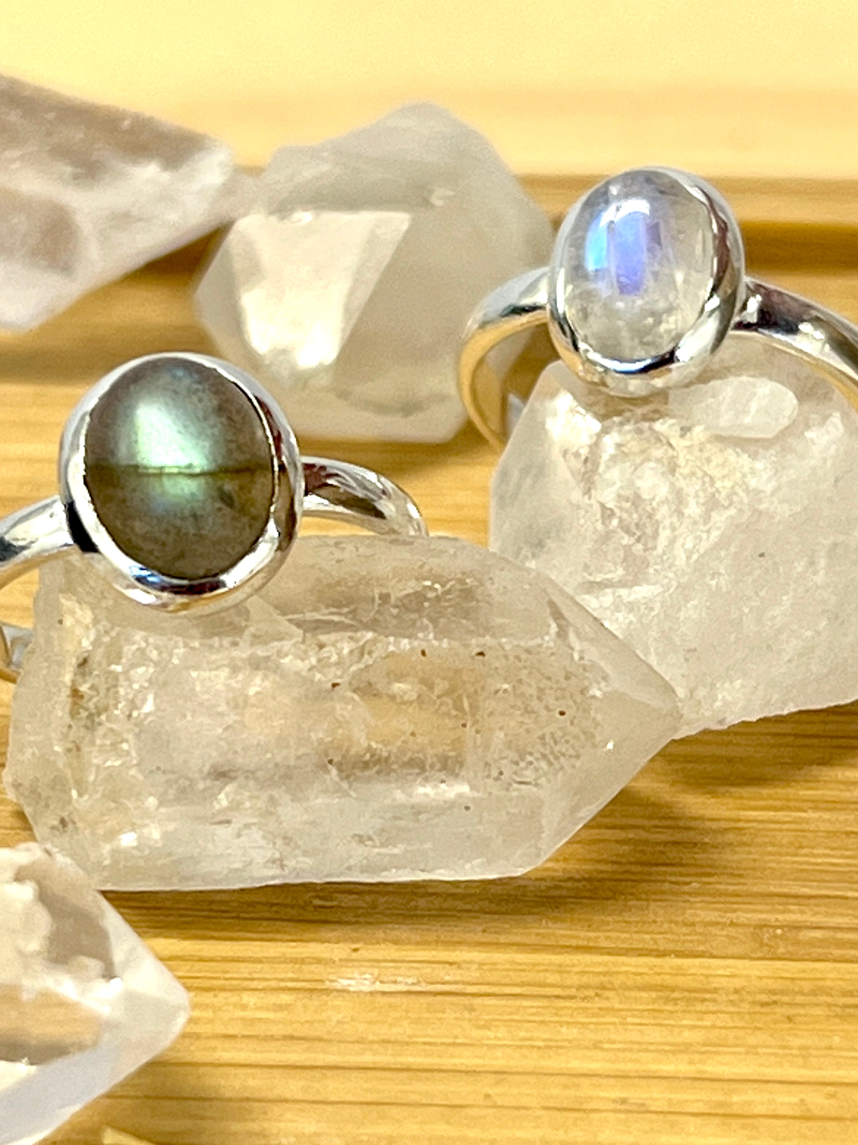 Three Simple Oval Moonstone Or Labradorite Rings with labradorite stones on top of a wooden table.