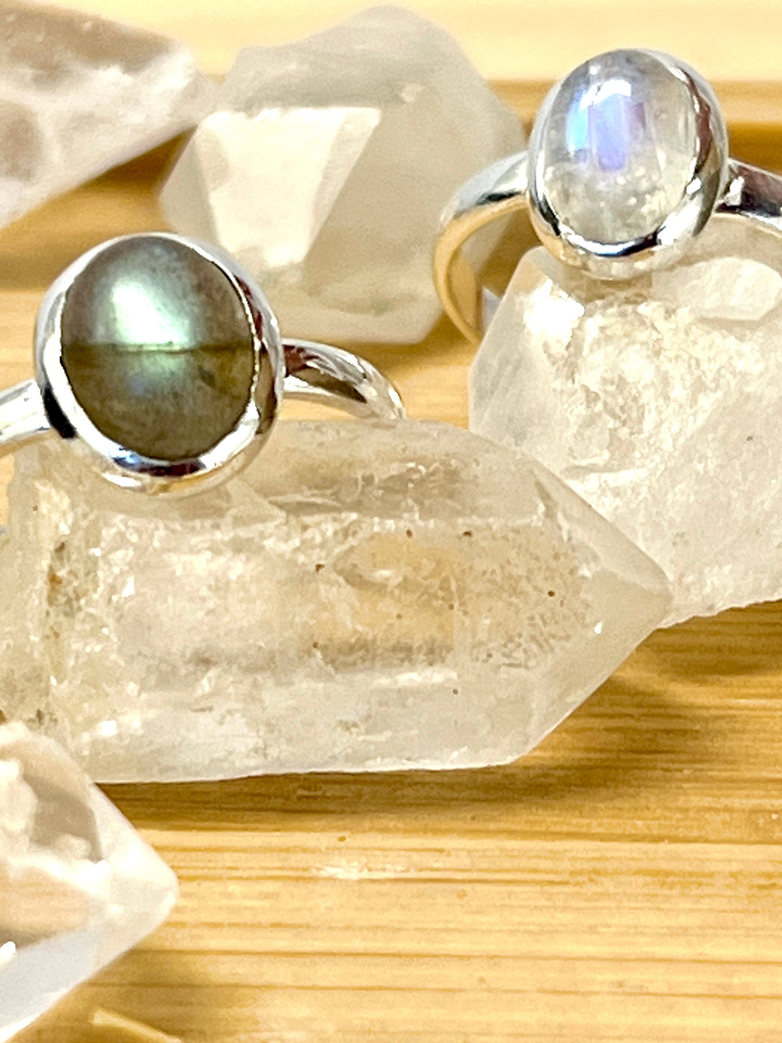 Two simple oval moonstone or labradorite rings set in sterling silver, displayed on a wooden table.