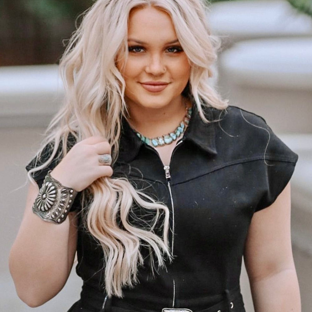 
                  
                    A woman with long blonde hair wearing a black outfit, accessorized with a Handcrafted Silver Concho Cuff, necklace, bracelet, and rings, stands outdoors.
                  
                